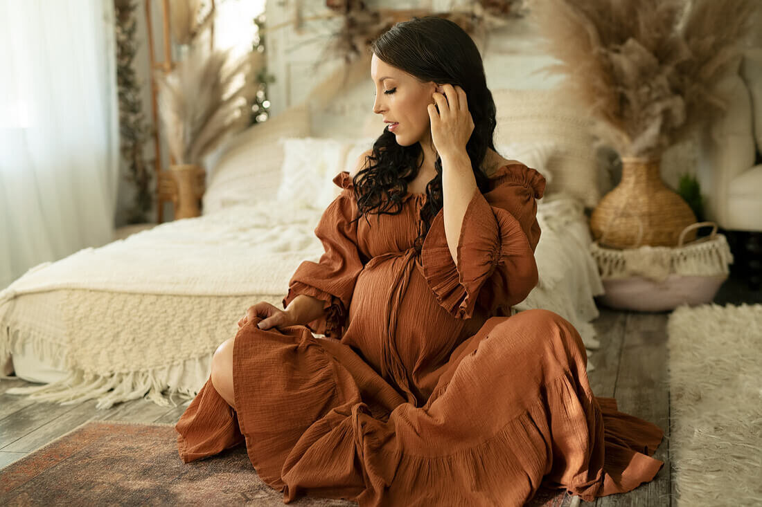 Pregnant woman tucking hair in cinnamon coloured dress