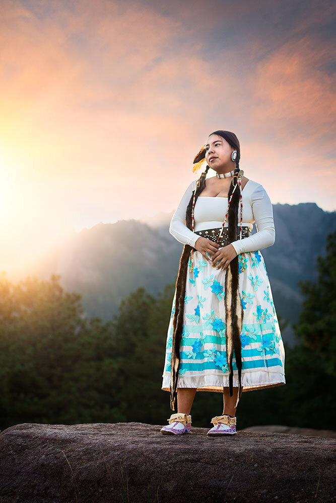 cotton-candy-clouds-native-american-senior-high-school-graduate-standing-on-rock-blue-flower-otter-mink-hair-shell-mocassins