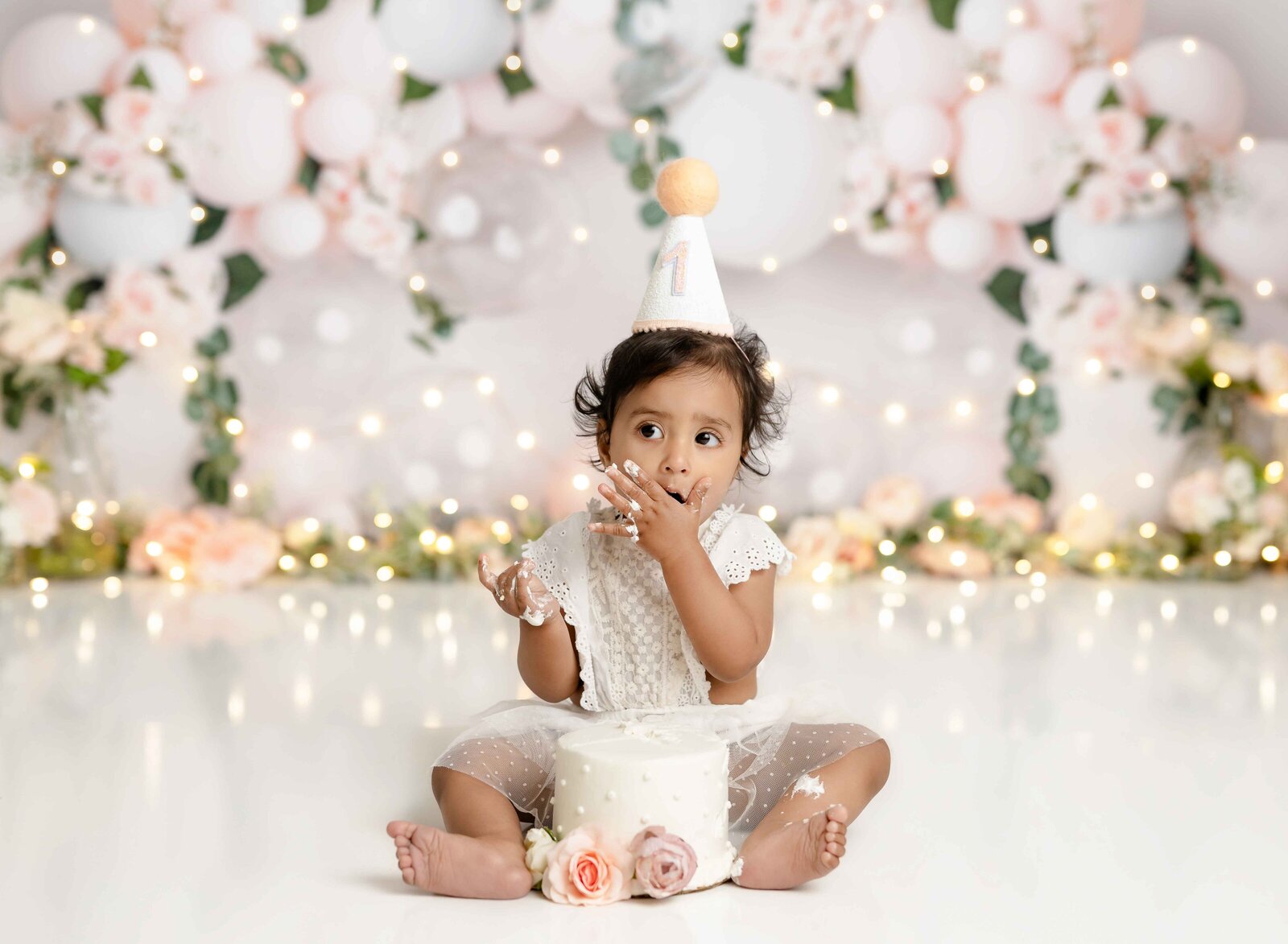 Baby girl sitting on floor and eating cake. Cake smash photo studio located near Atlanta, GA.