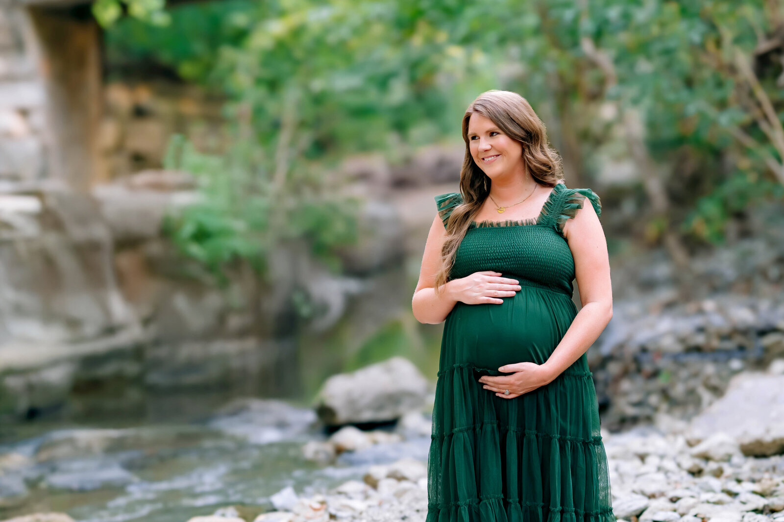 Pregnant mother in a green dress standing near the water during an outdoor maternity session in Prosper, Texas, captured by Jennifer L. Kirk Photography.