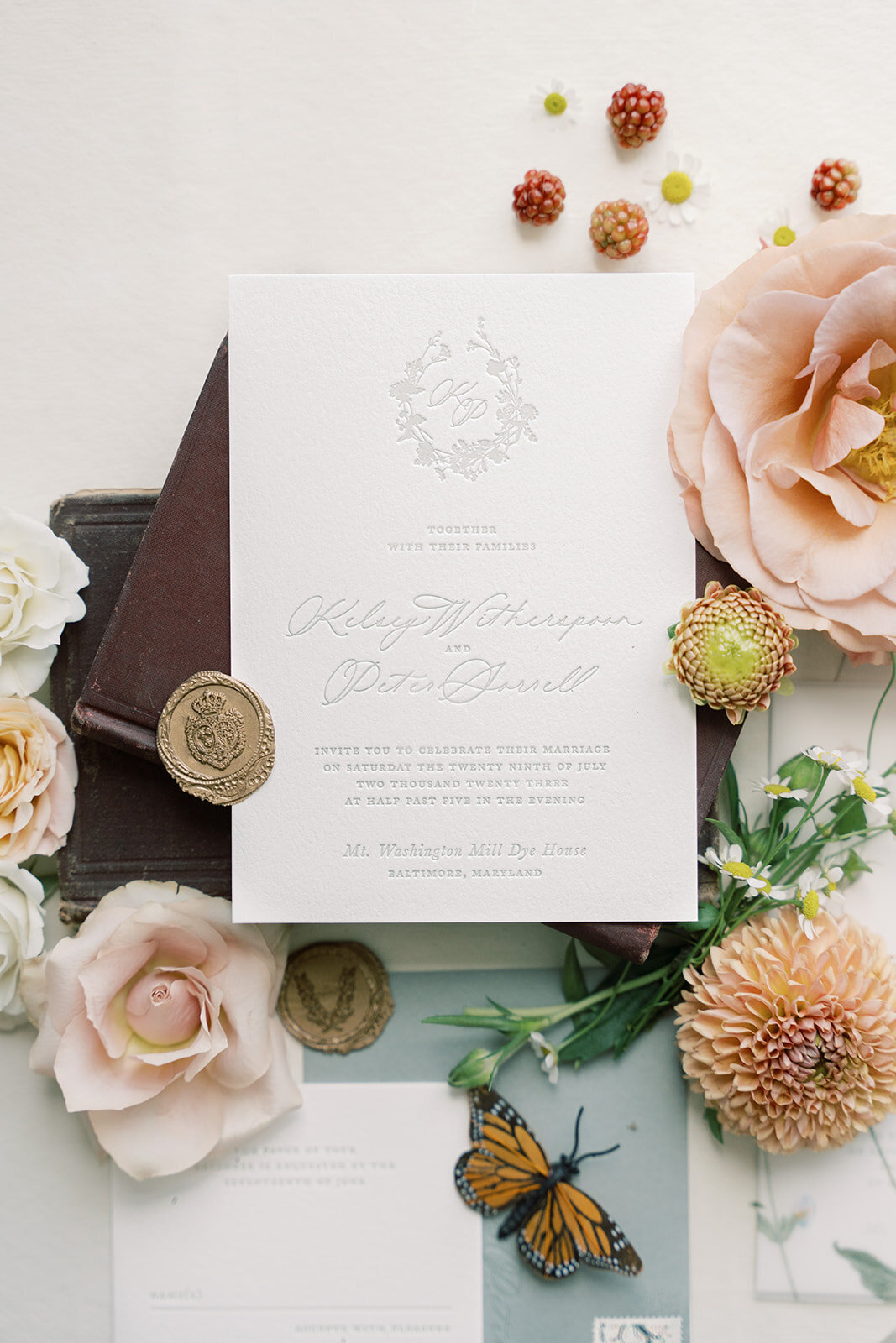 Flat lay invitation with floral accents such as peach dahlias, blush and peach garden roses and daisies.