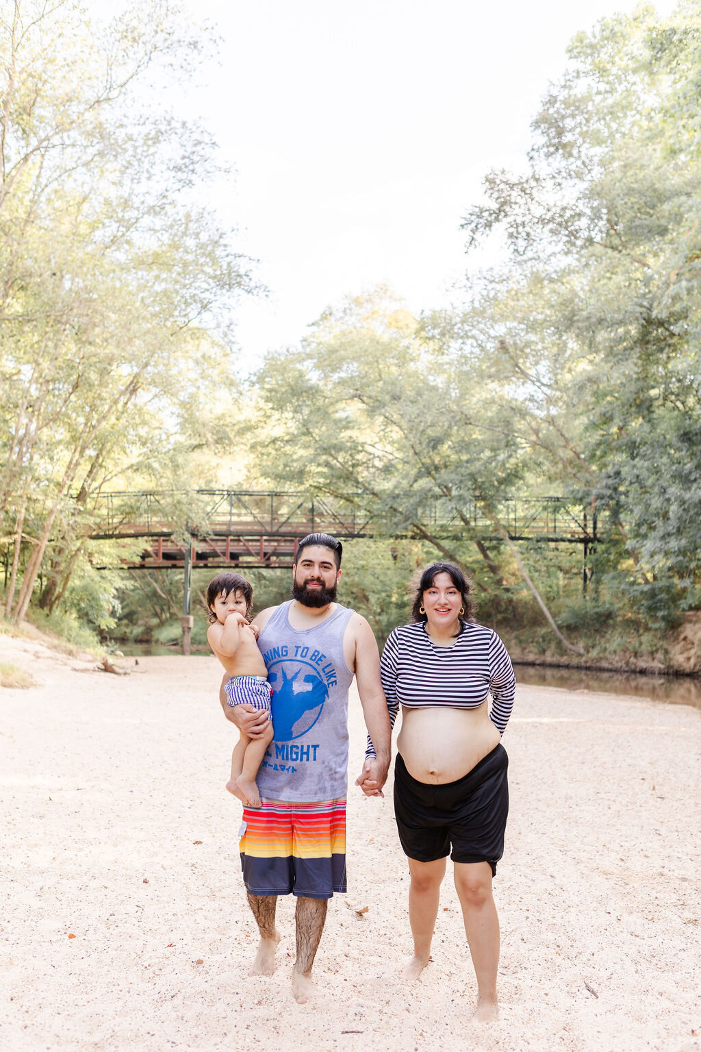 Maternity session at Lake Houston Wildersness Park
with the family standing in the sand while father and mother hold hands and toddler is being held in the fathers arms  