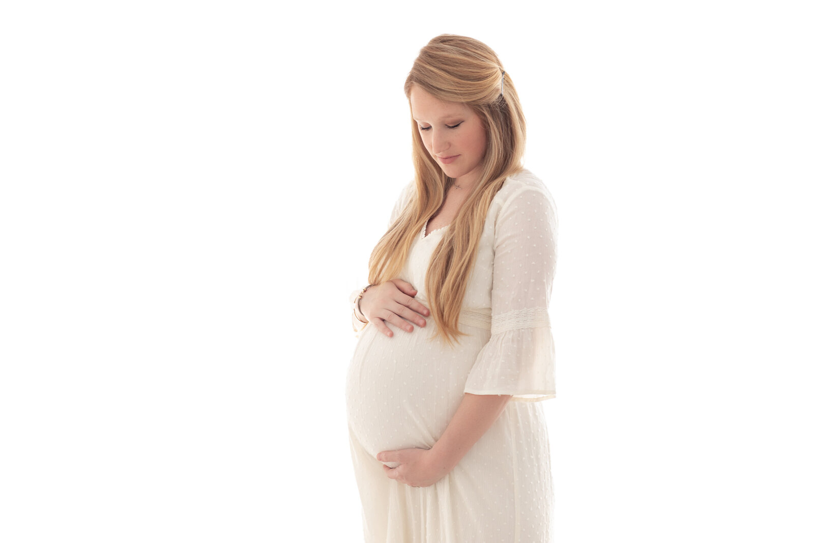 Pregnant woman in a soft white dress gently holding her belly