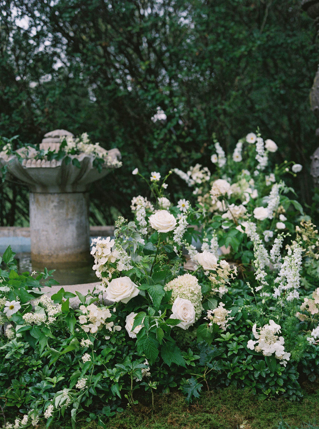 Florals covering water fountain at the Evergreen Museum ceremony including white larkspur, white quick-fire hydrangea, white Japanese anemone, white lisianthus, white garden roses and lush organic greenery.