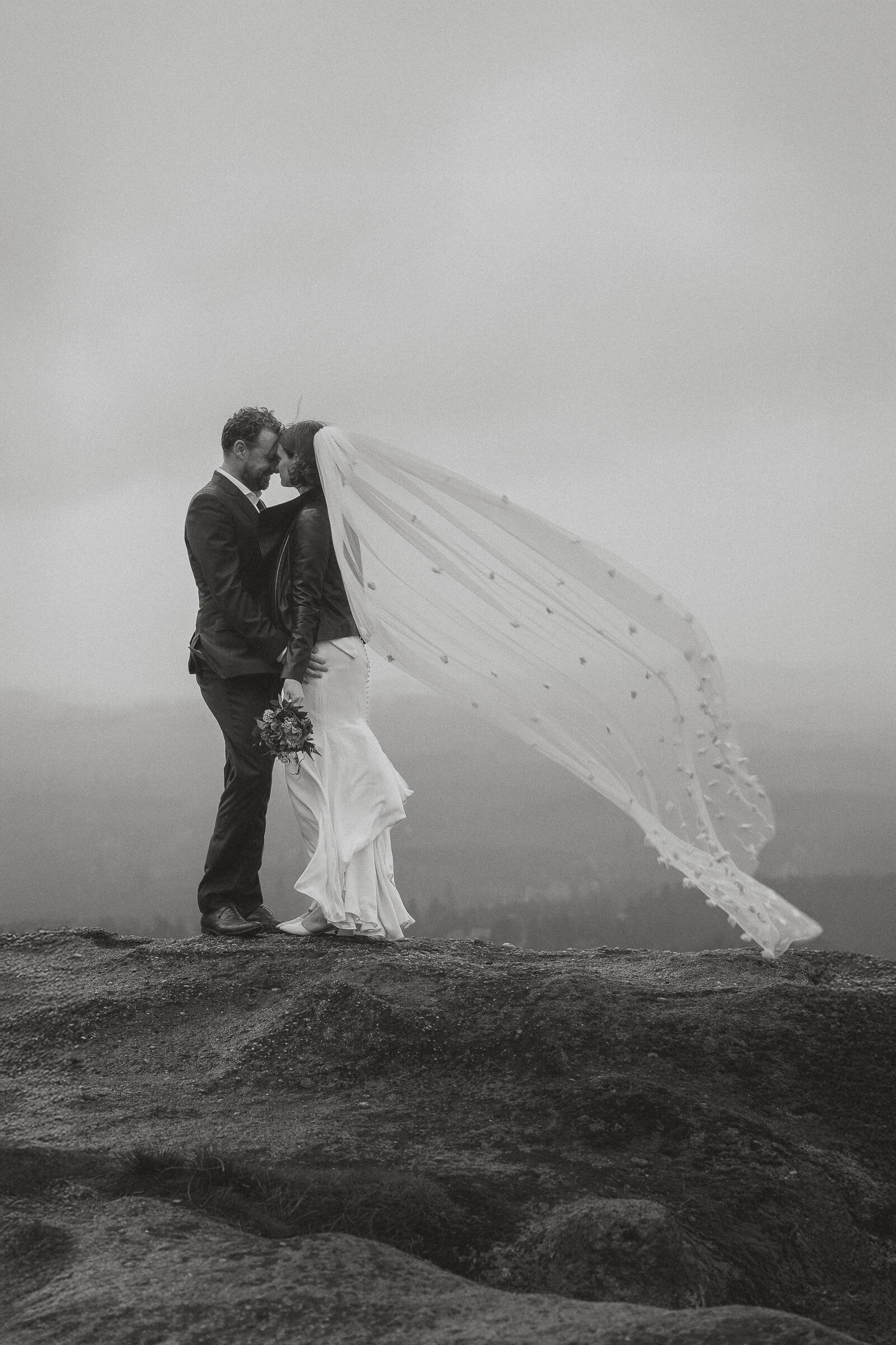 Bride and Groom with veil flying in the wind at Little Mountain in Errington during wedding portraits by Latitude 49 Photography