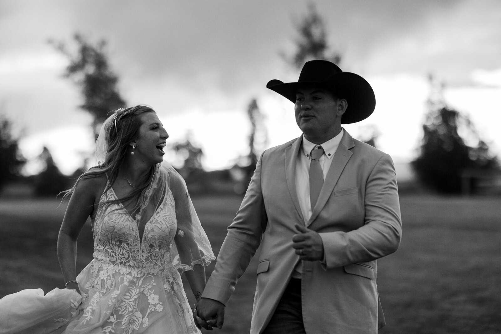 Joyful black and white image of the bride and groom walking hand in hand and laughing at their wedding in Loma, Colorado