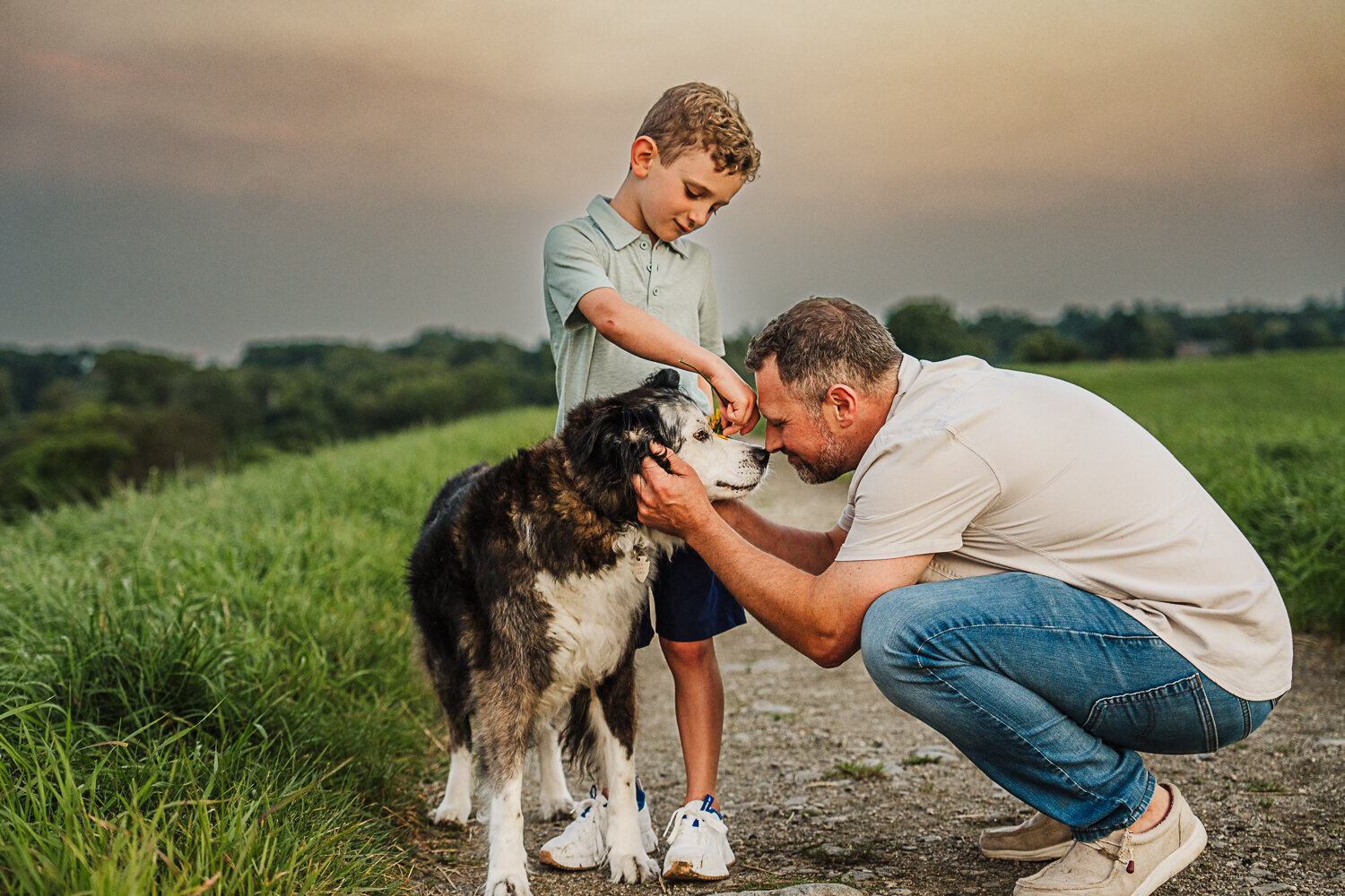 dad and son bend down to kiss elderly dog on the nose