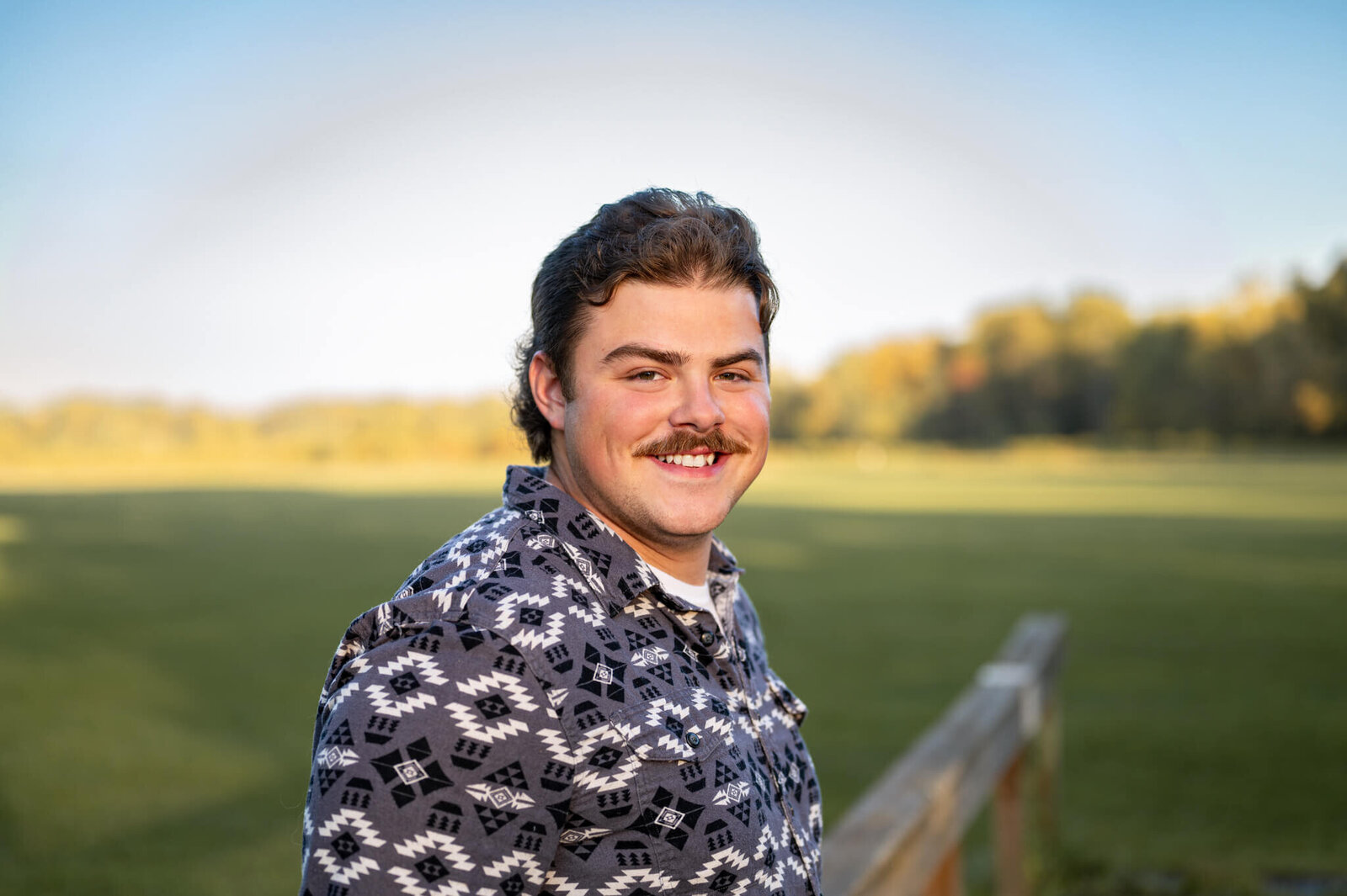Young man smiles at the camera in front of an open field of grass