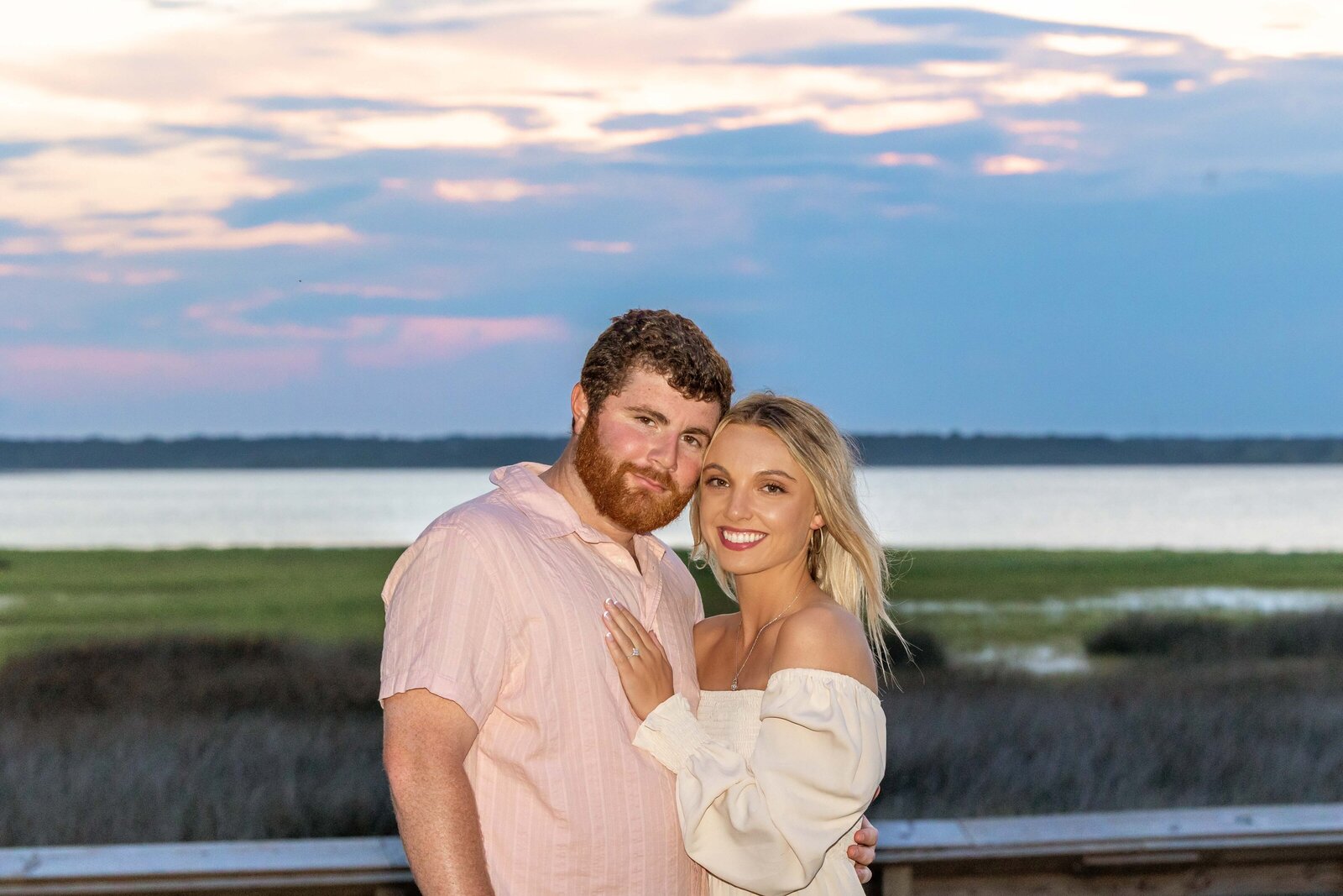 An engaged couple posing together against a stunning sunset backdrop in Wilmington, NC, with the water reflecting the evening colors. This romantic photo captures the essence of authentic wedding photography, perfect for couples seeking the best wedding photographer in North Carolina.