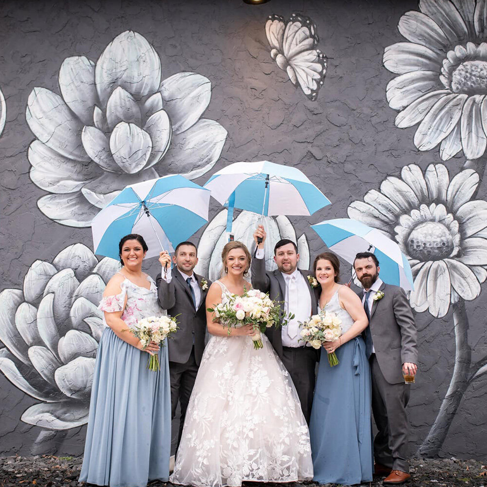 bridal party with umbrellas stand by black and white floral mural wall