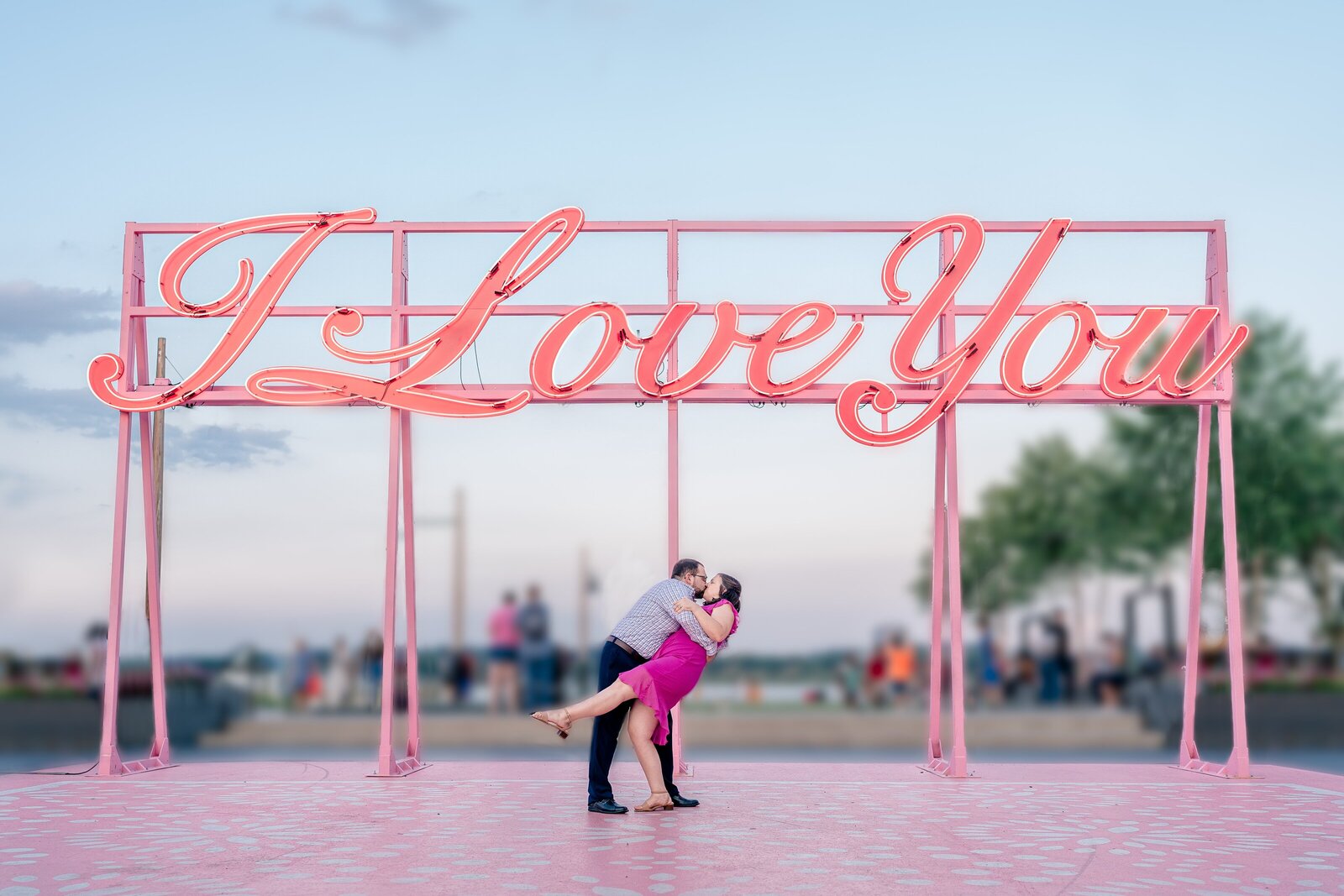 An engaged couple shares a kiss under a sign that says I Love You during their engagement session in Old Town Alexandria