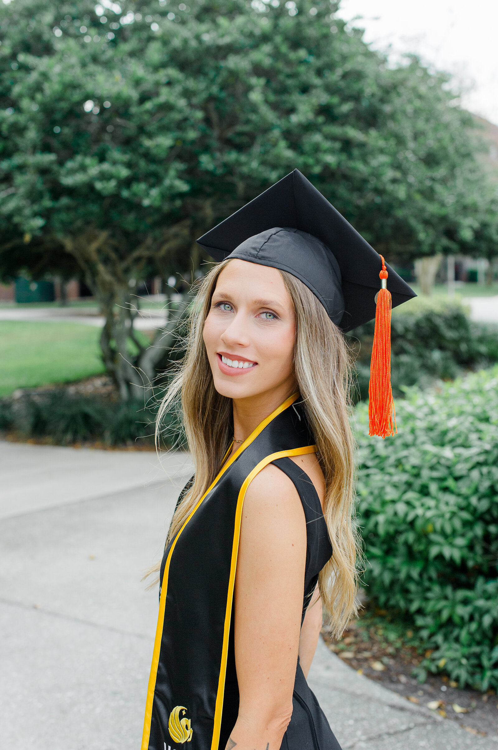 UCF senior girl smiles at camera in cap and gown in front of engineering buidling