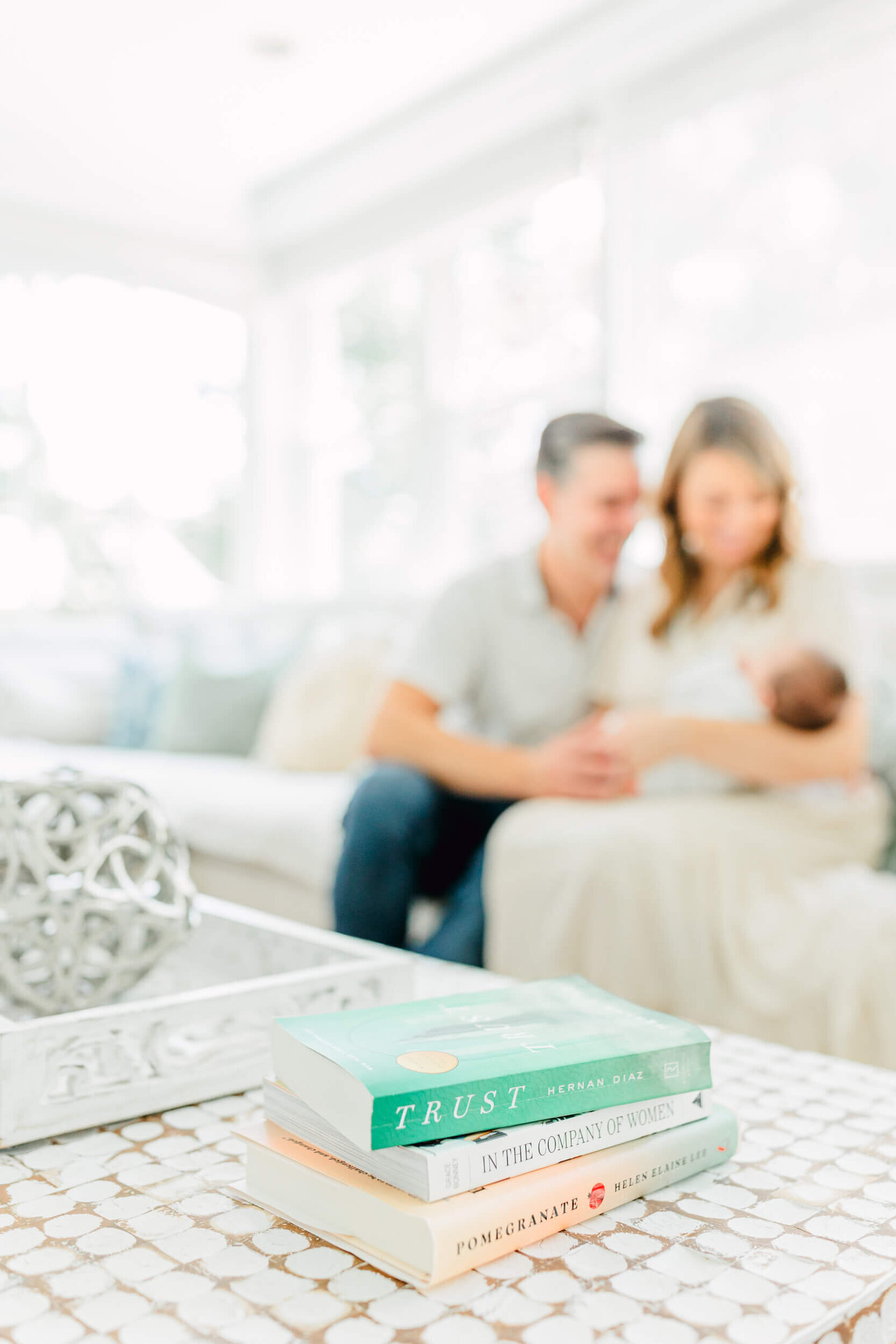 Artistic focus on a book named "Trust" with parents and newborn blurry in the background