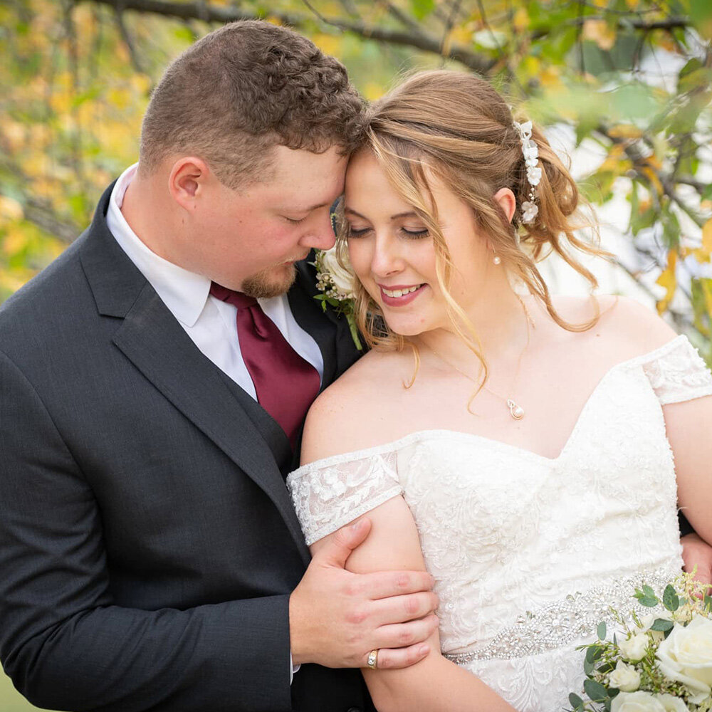 wedding couples snuggles heads together under fall leaves
