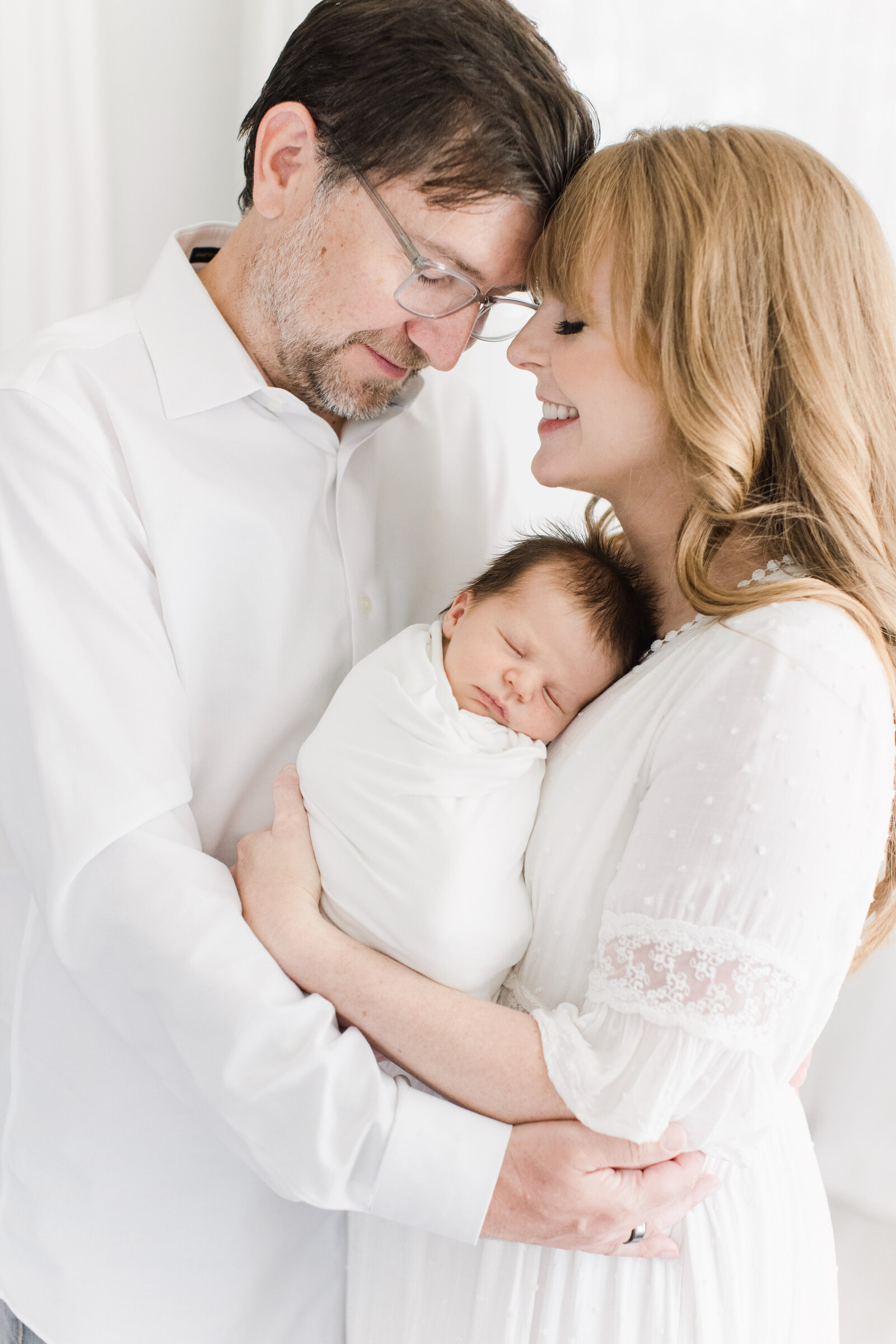 Parents with newborn baby boy in all white studio.