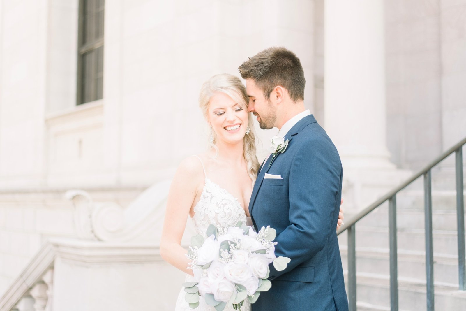 A groom nuzzles into his bride's temple as she smiles with closed eyes. They are on the steps of the James J. Hill House before their Landmark Center Wedding.