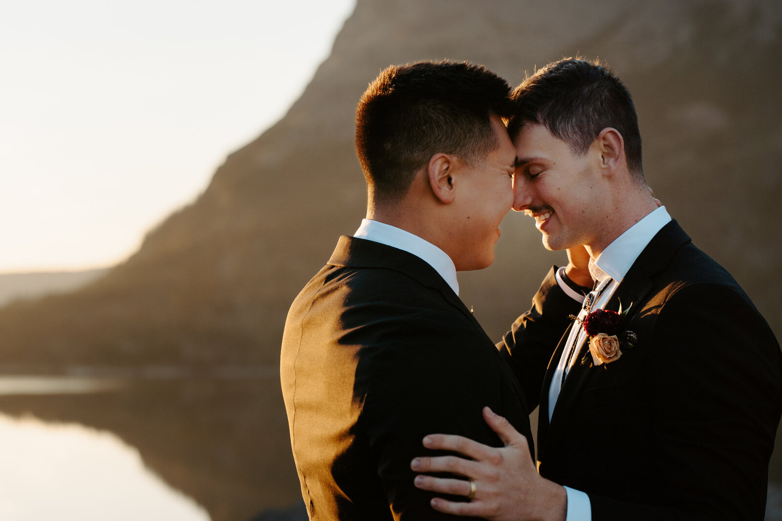 Two grooms resting their foreheads together at sunrise