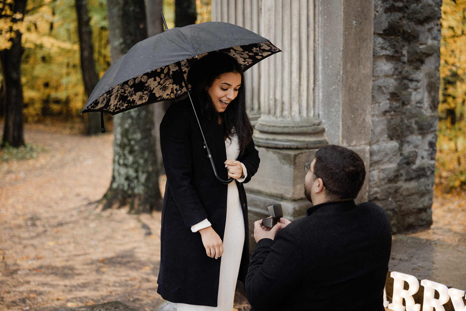 A man on one knee, proposing to his shocked and happy girlfriend.
