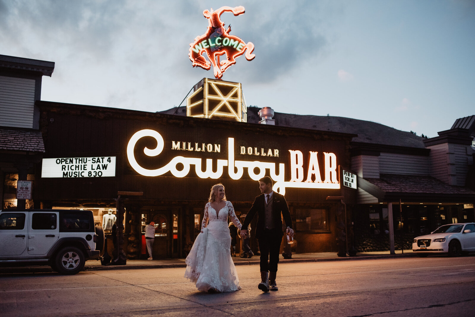 jackson hole photographers photographs bride and groom holding hands and walking across the road in downtown jackson hole in front of cowboy bar