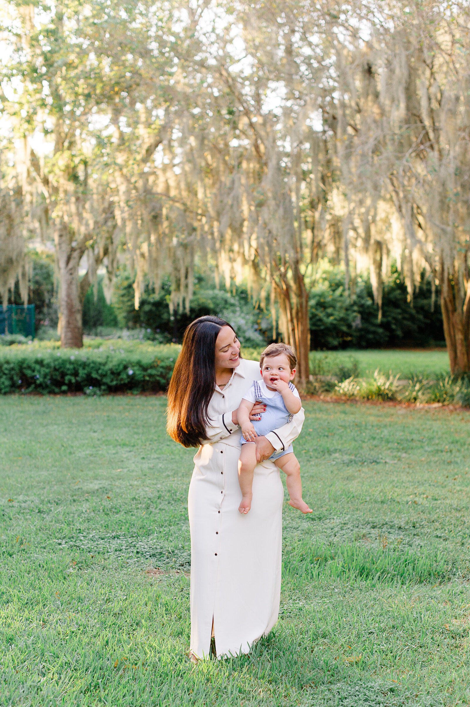 Mom wearing a beautiful white classy dress while holding her cute son in a park in Vero Beach