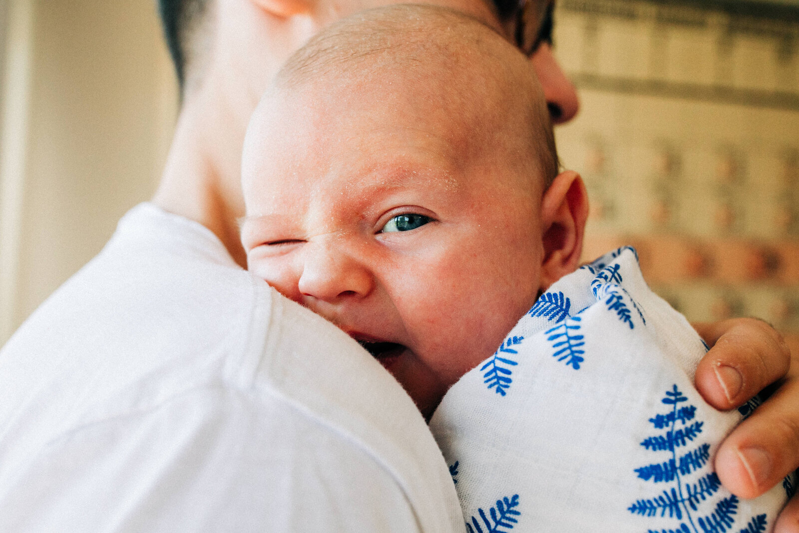 dad holding newborn baby boy in blue and white swaddle who is winking at the camera