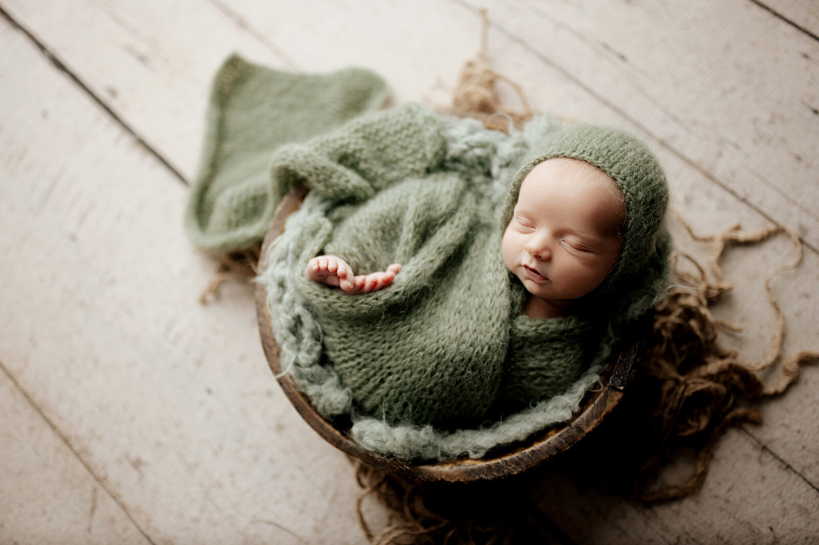 Newborn baby boy in a basket with a green wrap in Lane Weichman Photography studio