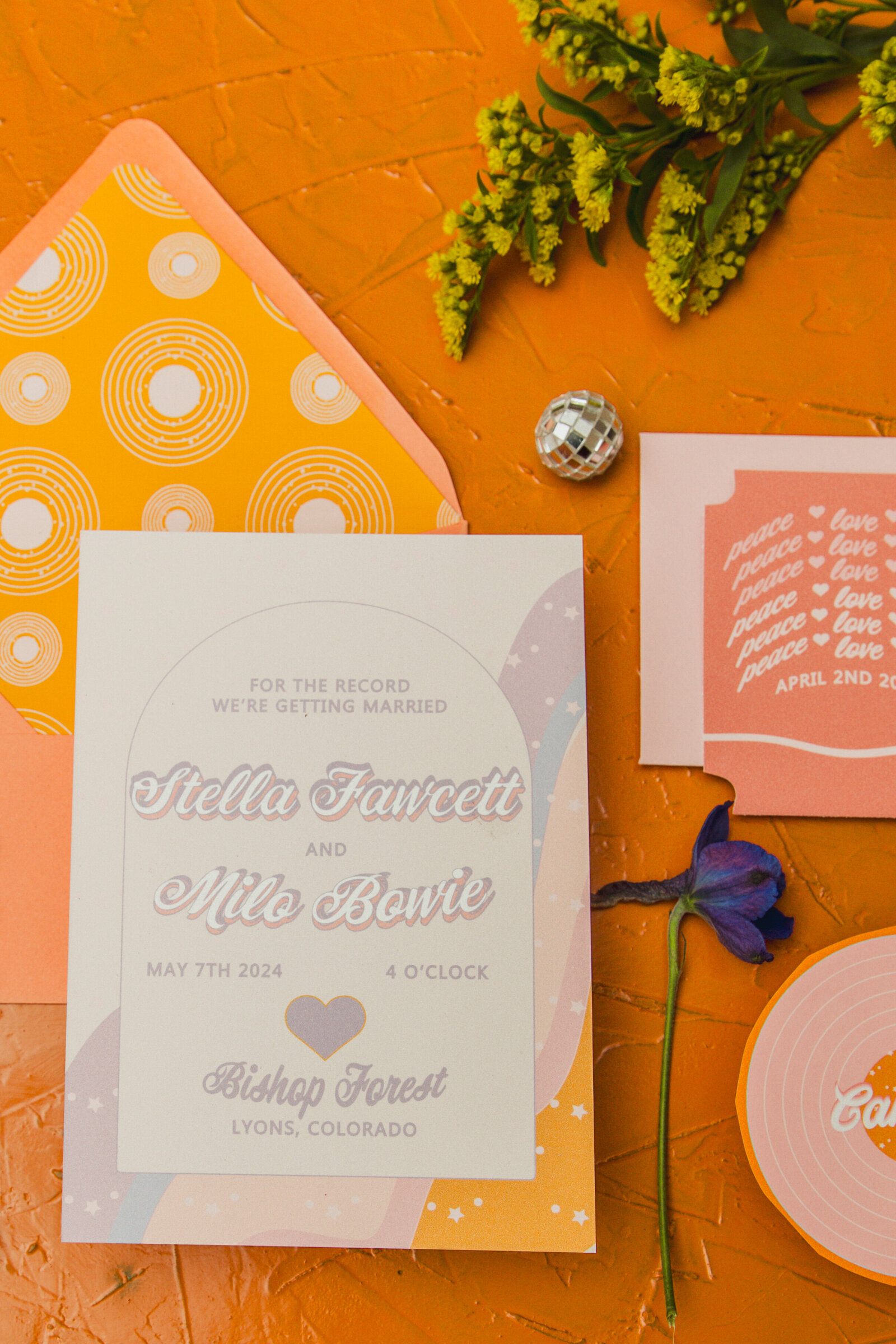 A close up of a colorful wedding invitation in front of a orange envelope with a decorative envelope liner.