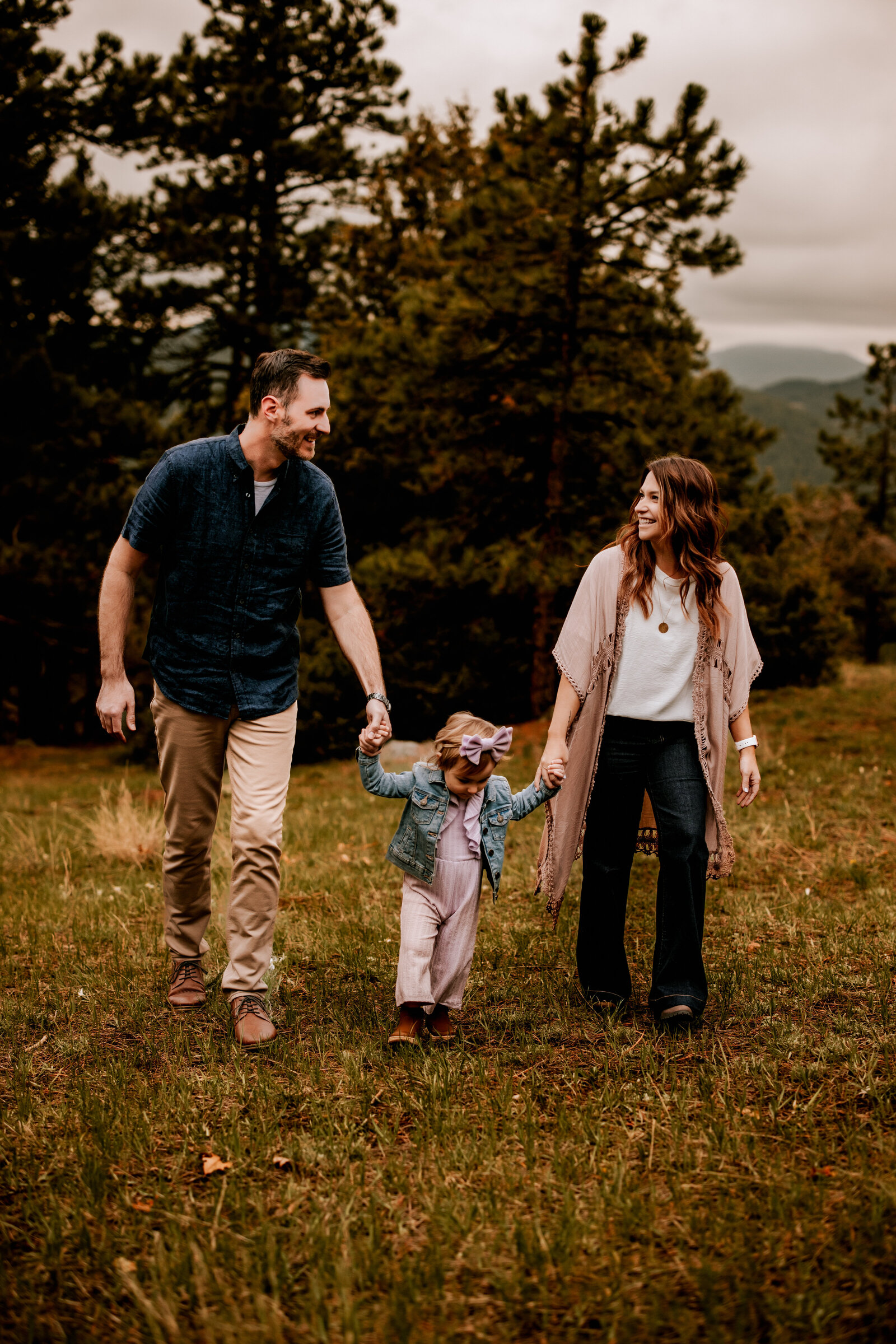 Family of three with small toddler hold hands whie walking up a  mountain side at golden hour