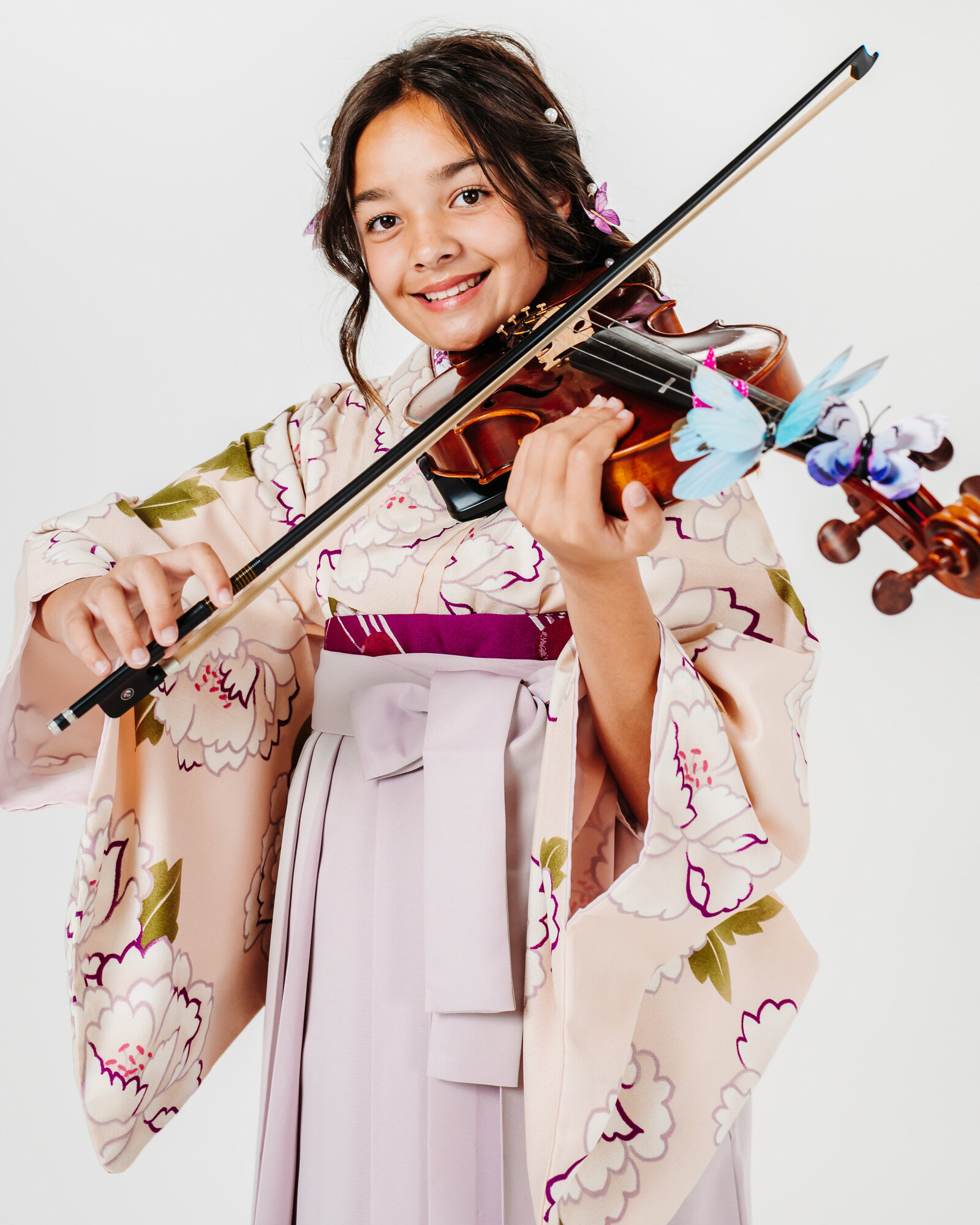 Girl in a pale pink and lavender hakama playing the violin decorated with butterfly accents for graduation | 卒業式 薄桃色とラベンダーの袴でバイオリンを演奏する女の子 蝶の飾り付き