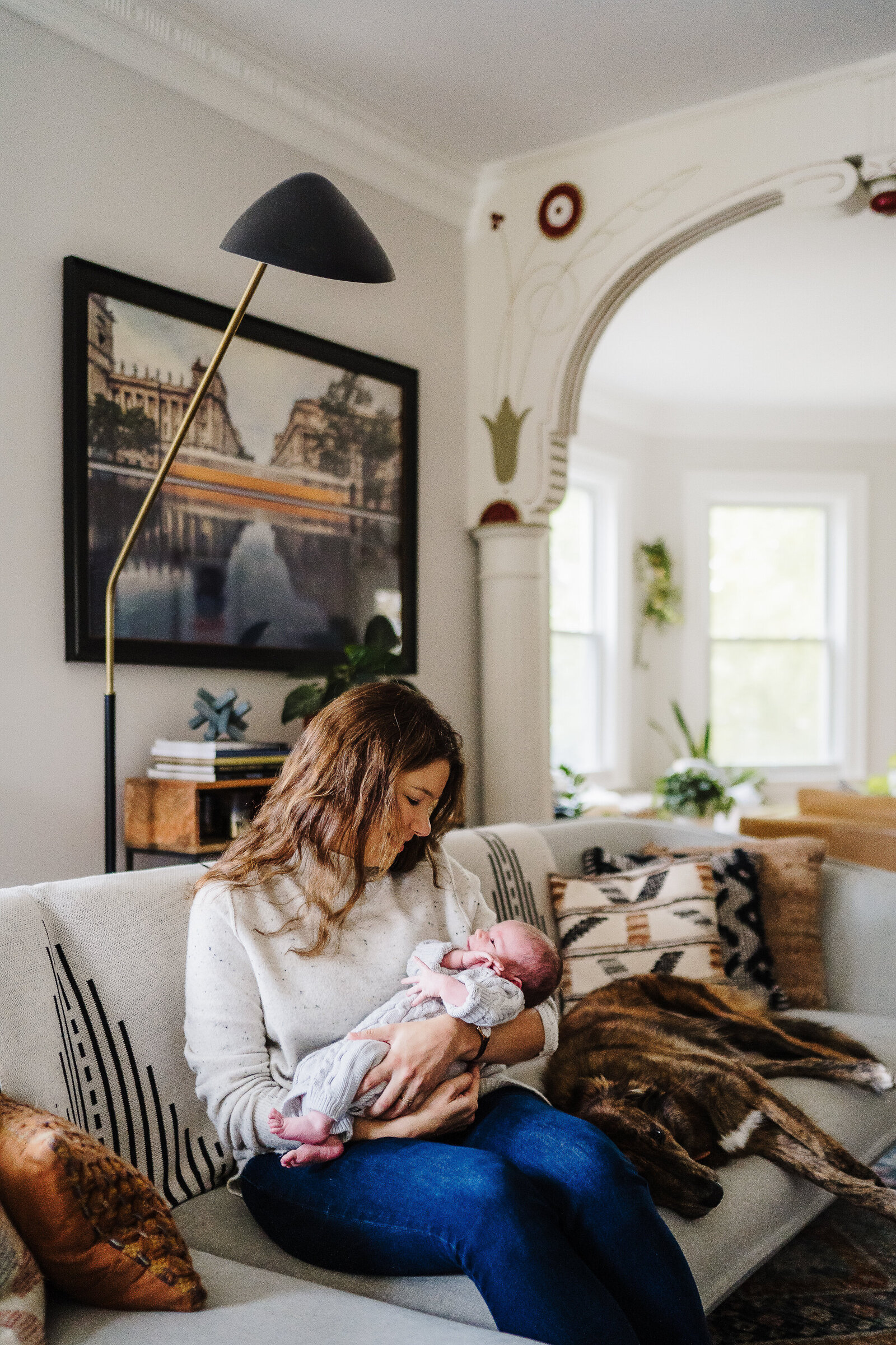 mom in mid century modern home looks at new baby boy on couch during newborn session