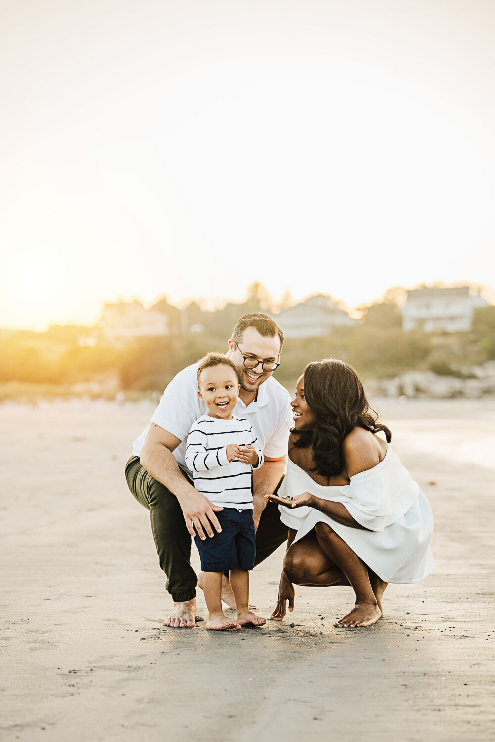 mom and dad laugh with toddler boy on beach at sunset