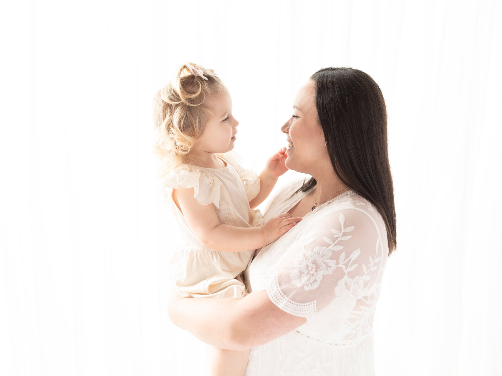 pregnant mother in white lace dress holding daughter for maternity portraits