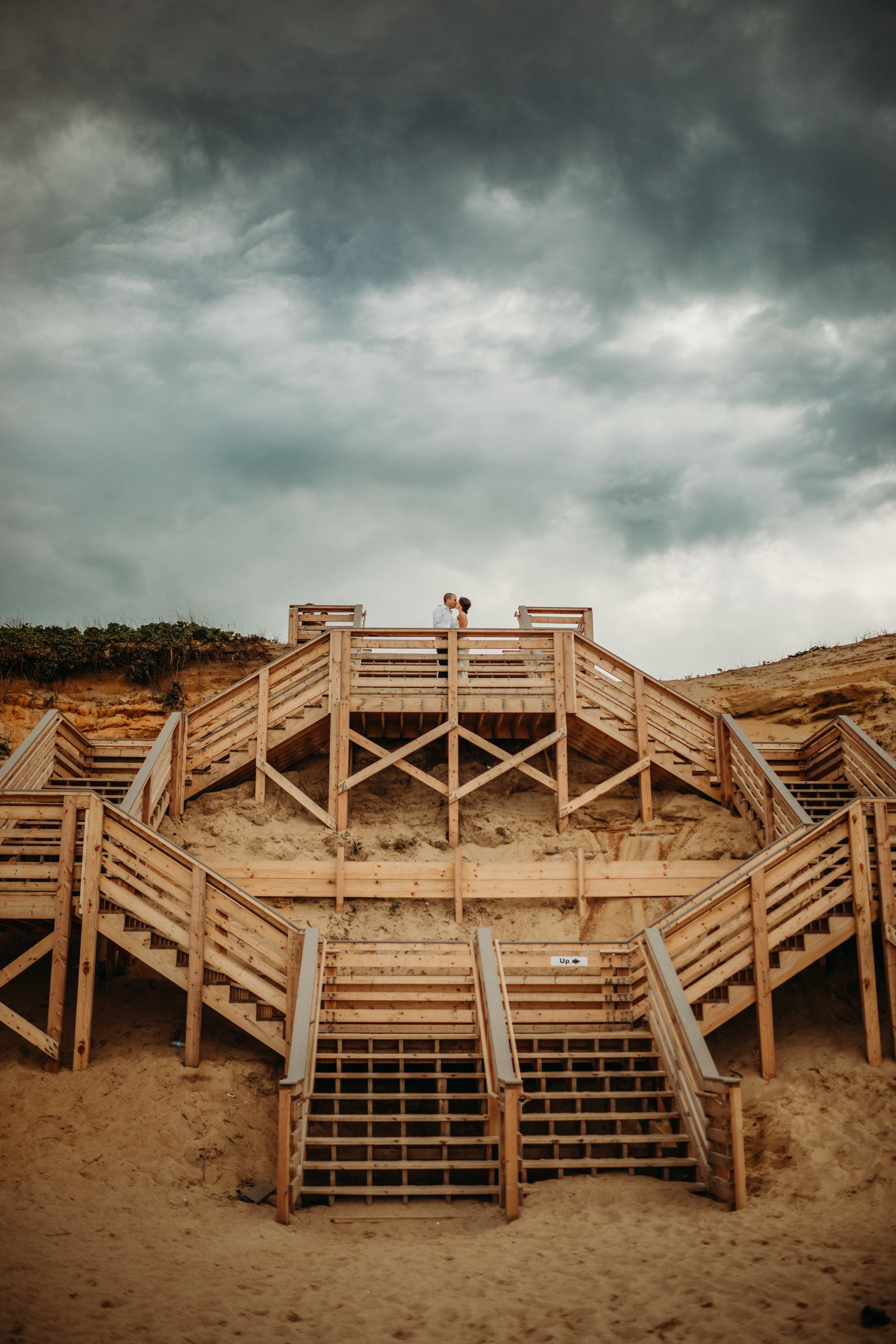 couple standing on wooden beach staircase with stormy skies