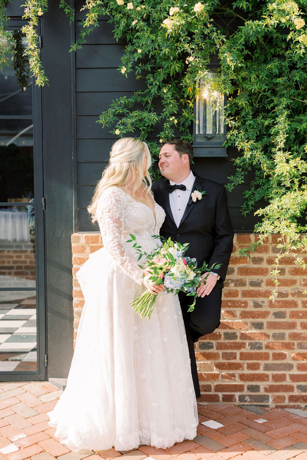 Groom looks at bride in white dress with brick background