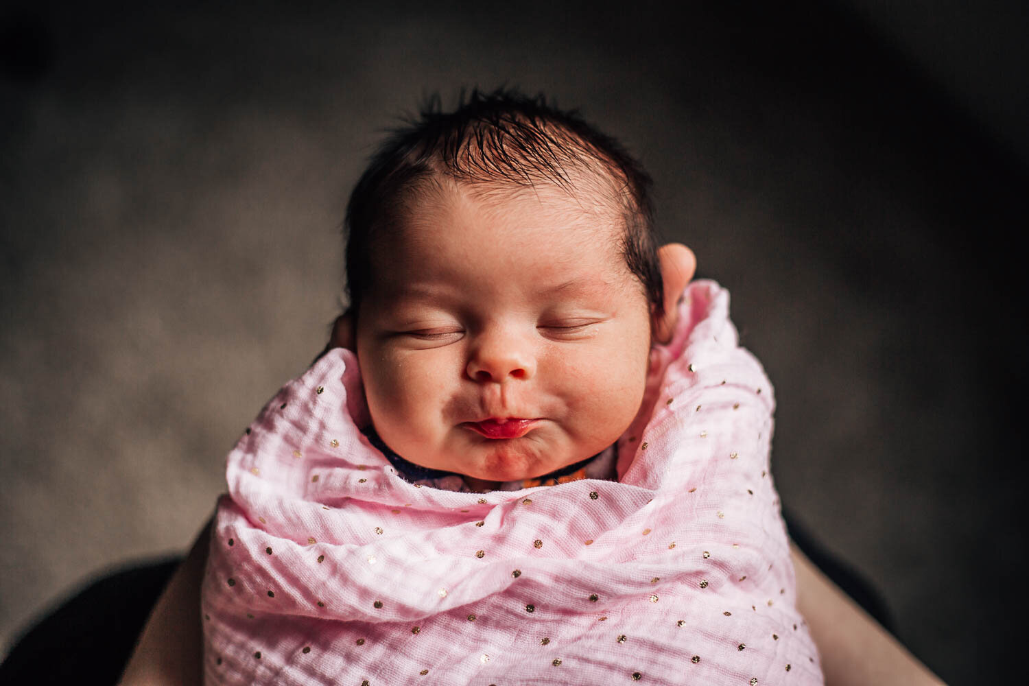 best newborn photographer in Hampton Roads captures a baby girl sleeping in a pink swaddle as her mother holds her