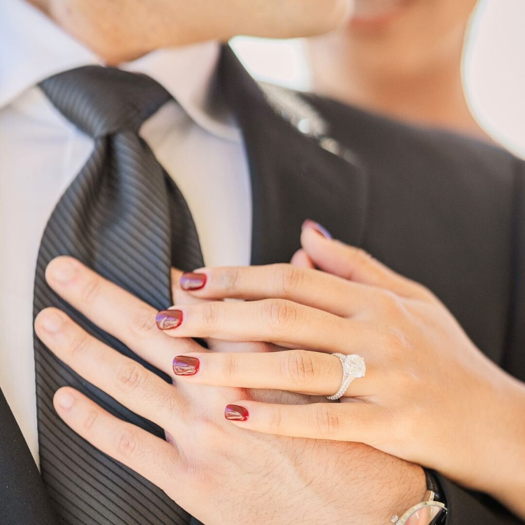 A bride and her groom place their hands on his heart showing off her diamond wedding ring.