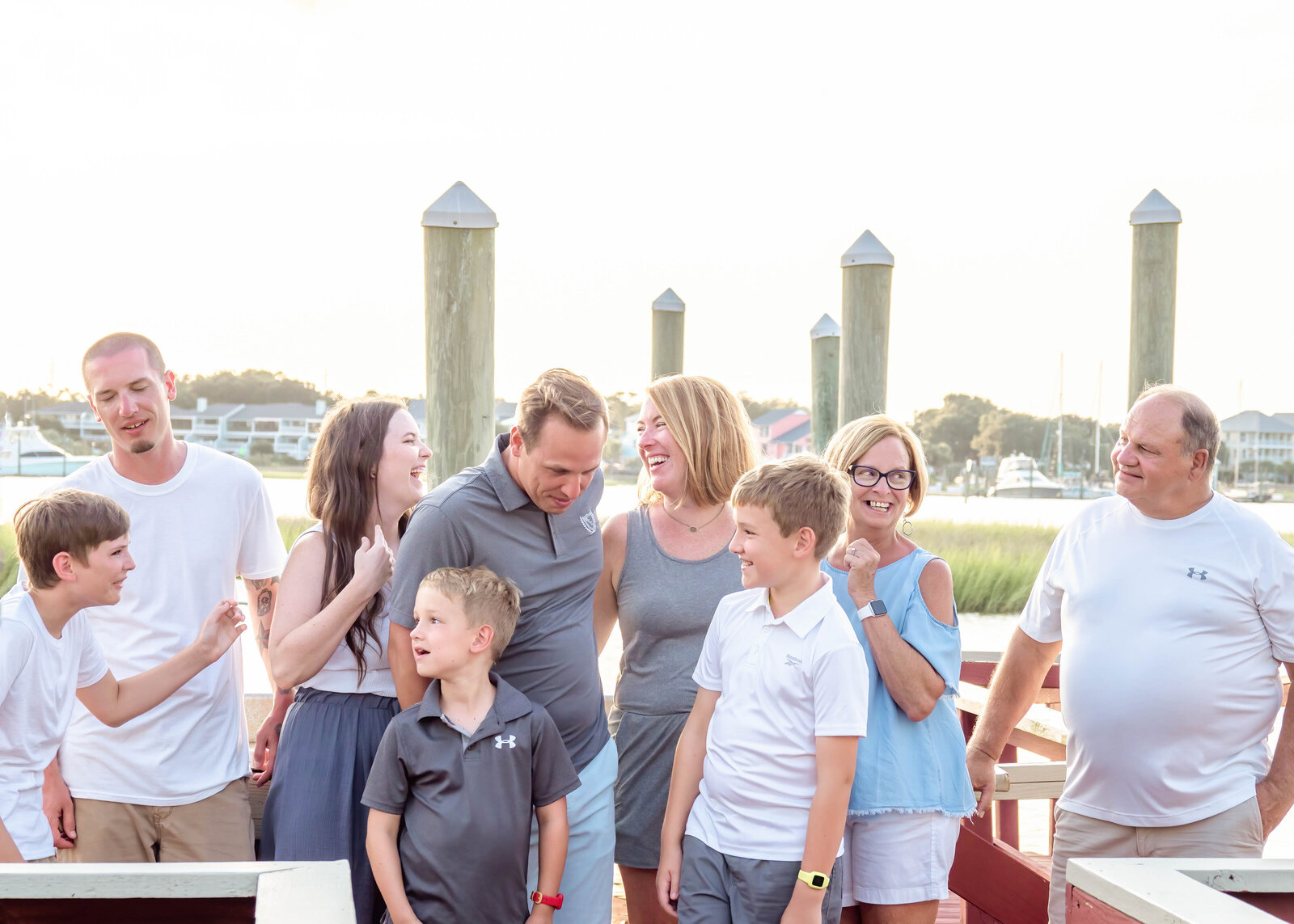 A family shares a joyful moment at a marina, with boats and dock posts in the background. Dressed in casual summer attire, they enjoy a relaxed atmosphere. Perfect for North Carolina family photography, capturing candid and happy interactions by the water.