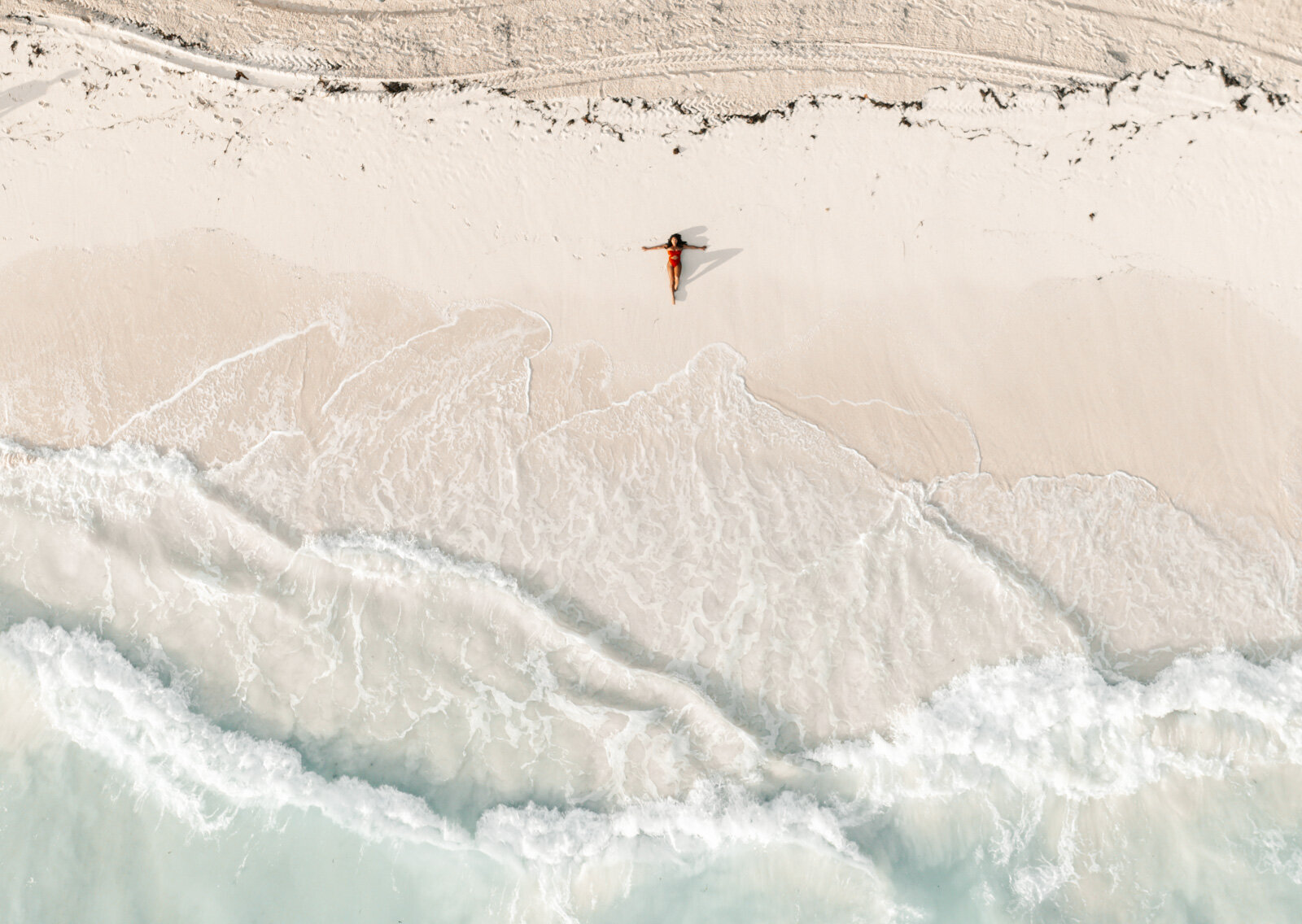 Drone shot of a woman  in a red swimsuit laying down face up on the beach