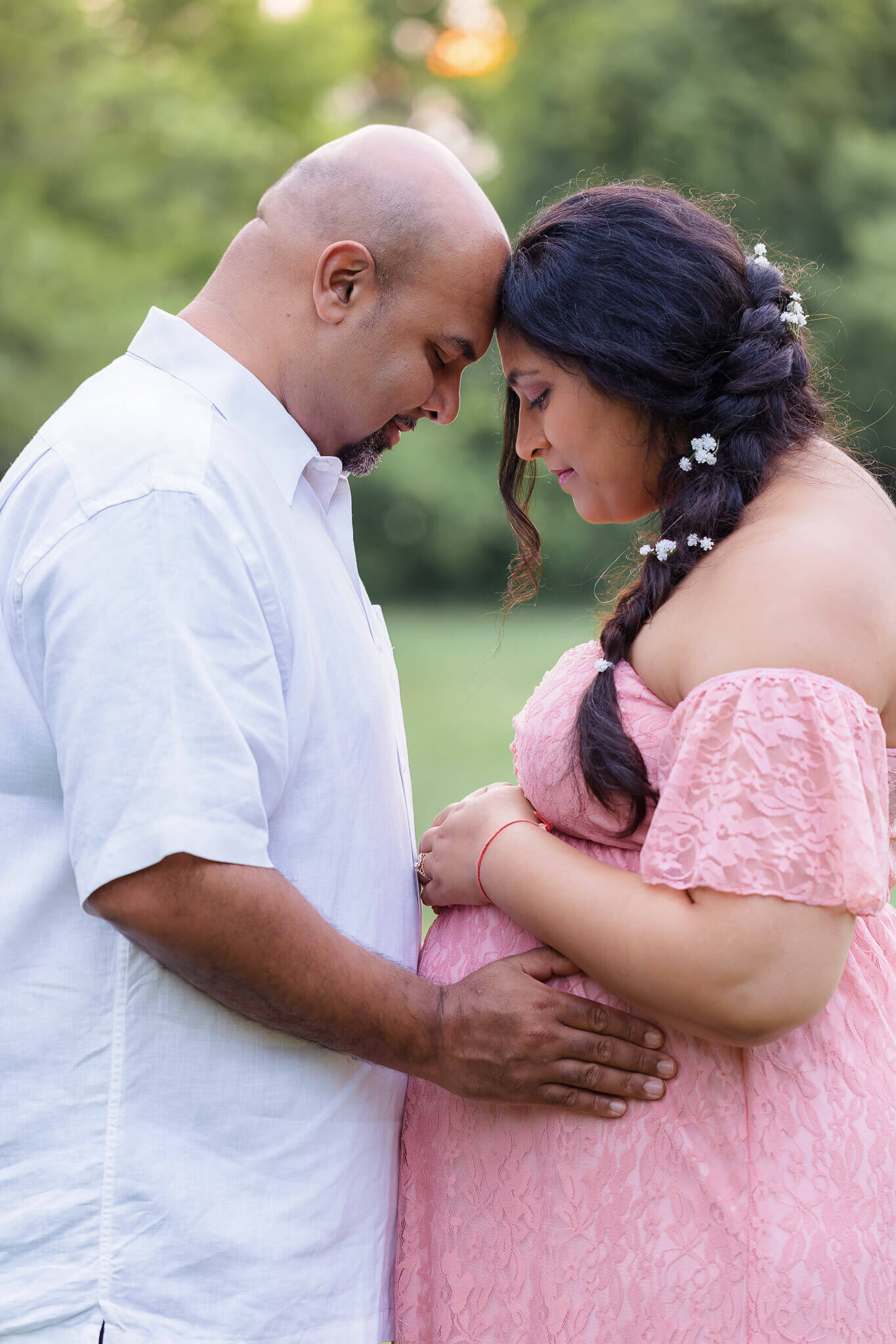 An expecting couple touching foreheads and hugging her belly.