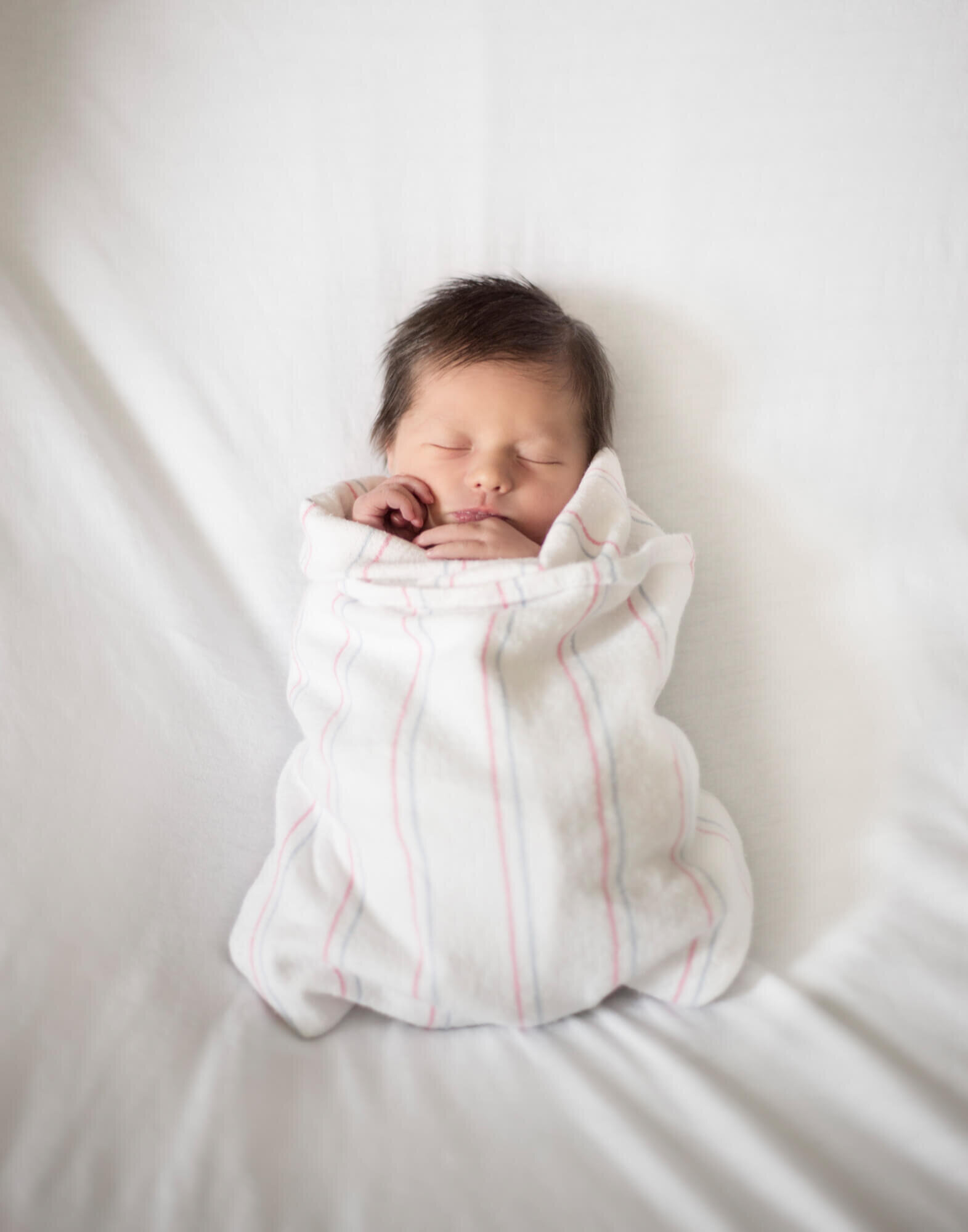 newborn baby girl with black hair wrapped in a hospital blanket