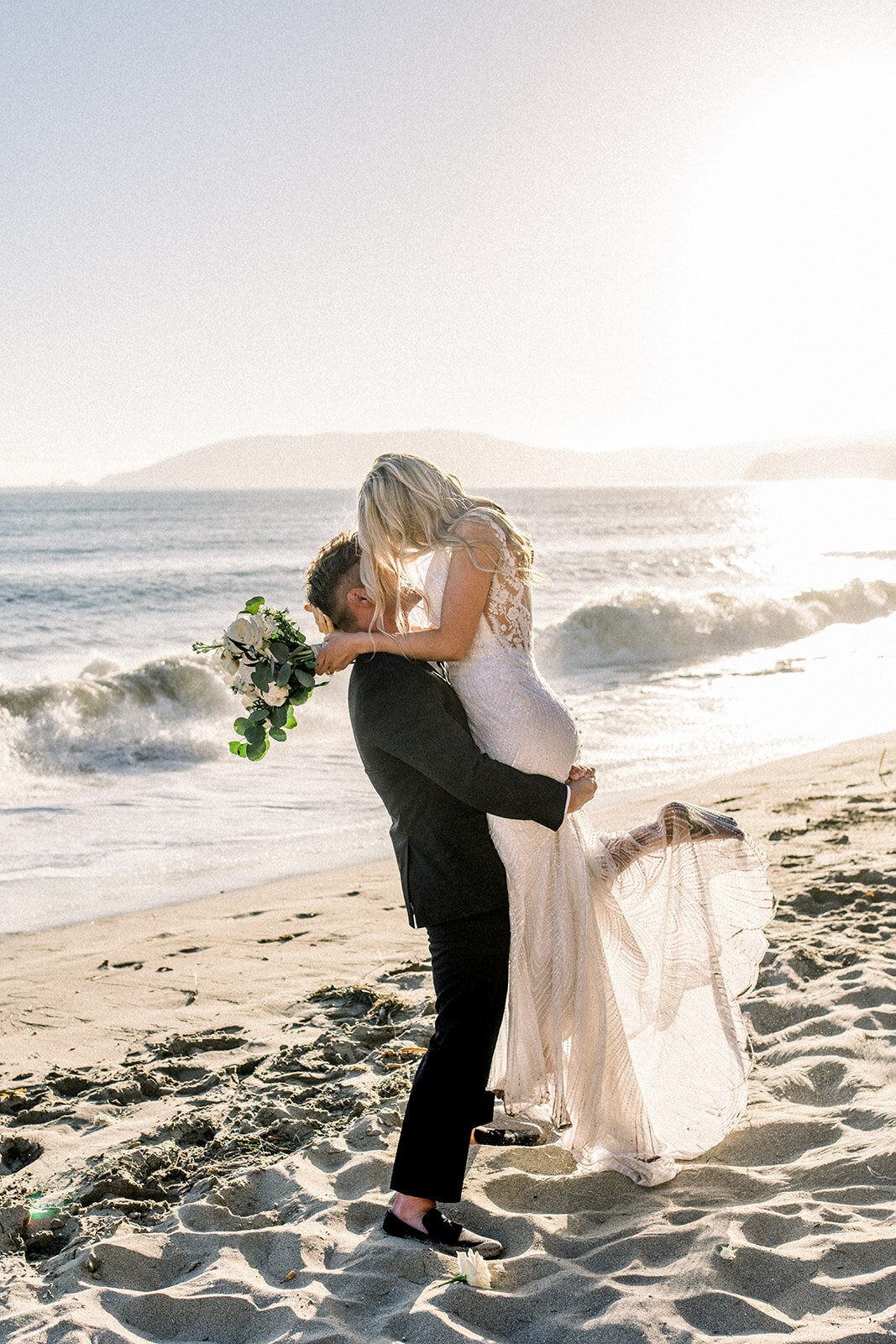 Groom lifting bride on the beach at Dolphin Bay Resort wedding in Pismo Beach, CA
