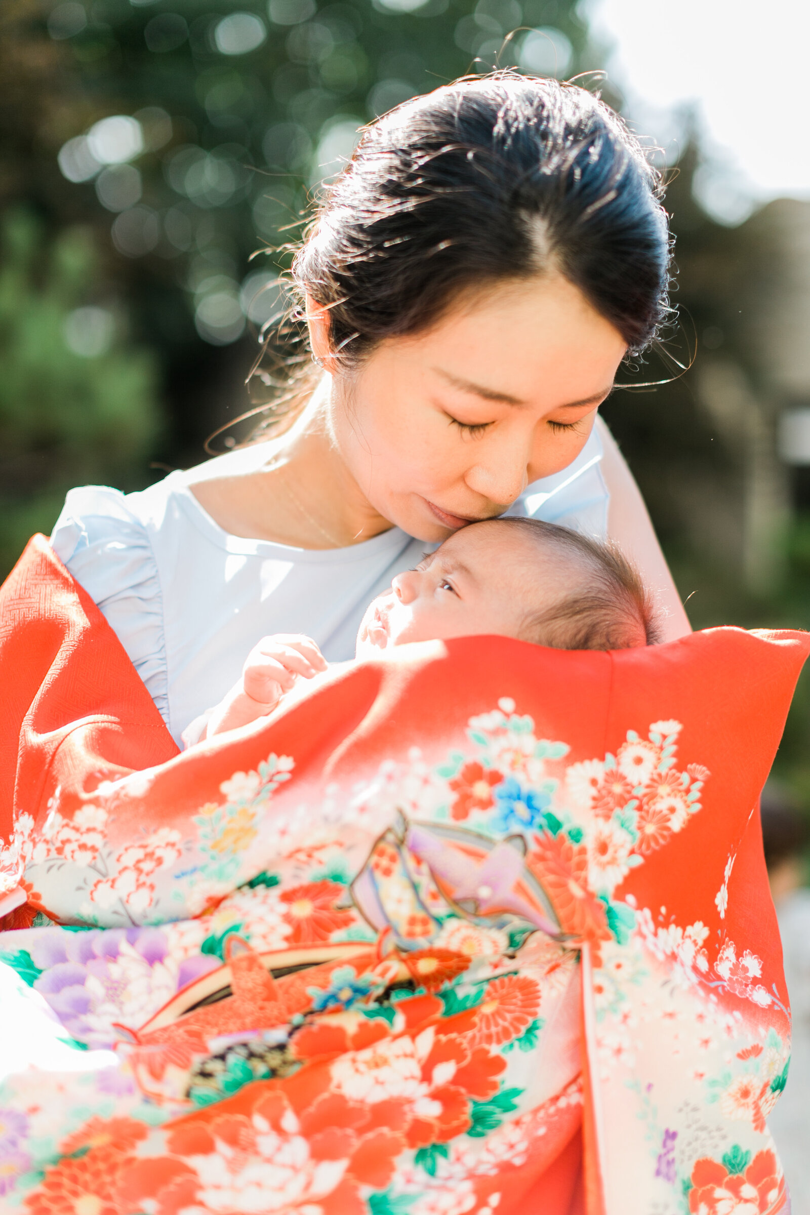 Mother kissing baby wrapped in vibrant red kimono during Hatsumairi ceremony | 初参り 母と赤ちゃん 赤い祝い着 ロサンゼルス
