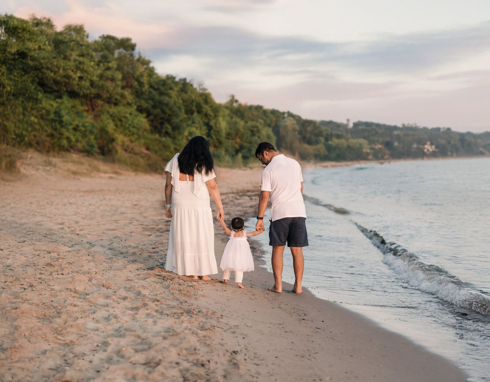 mom and dad holding daughters hand walking on beach
