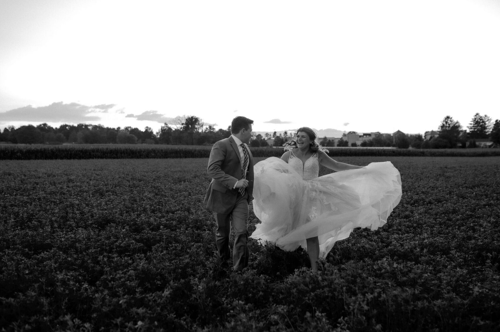 bride twirling wedding dress and frolicking in field with groom