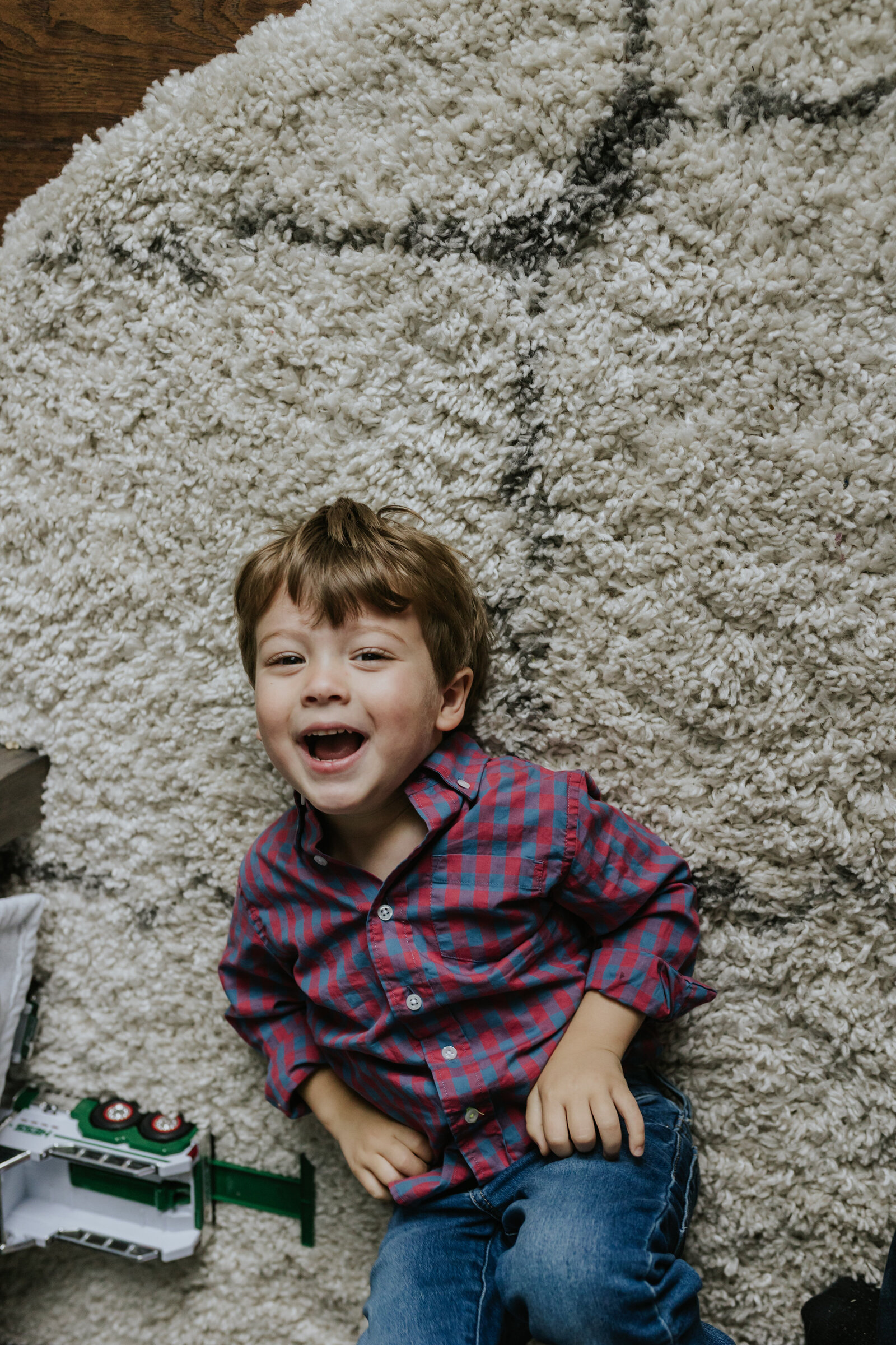 A young boy lays on his back on a shag rug and laughs