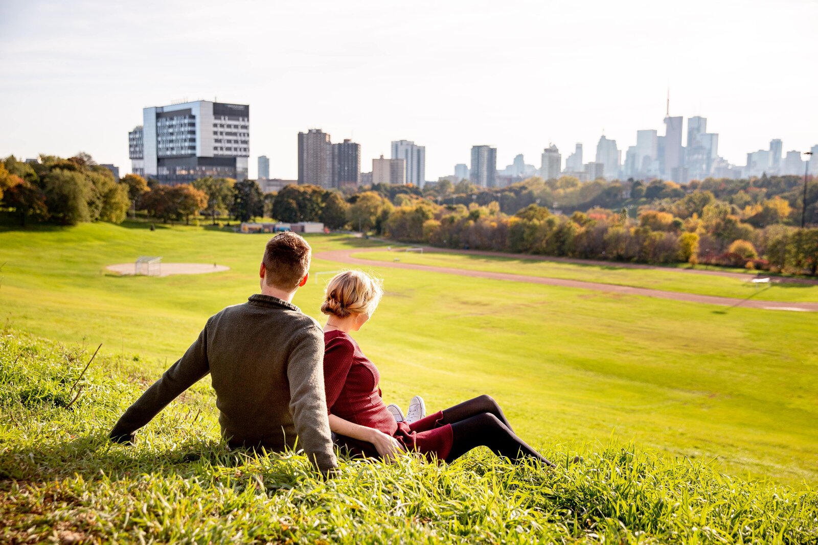 Couple sit in the park atop Riverdale Park during their Toronto engagement session.
