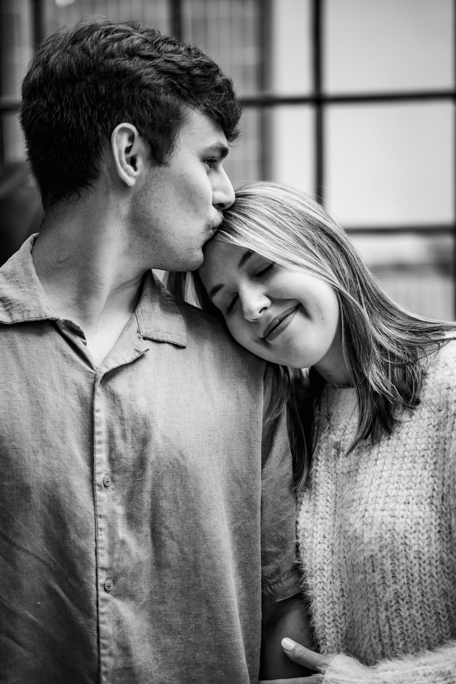 Black and white shot of Luke kissing the top of Megan's head during their engagement session at Comeback Coffee in Memphis, capturing a tender moment.