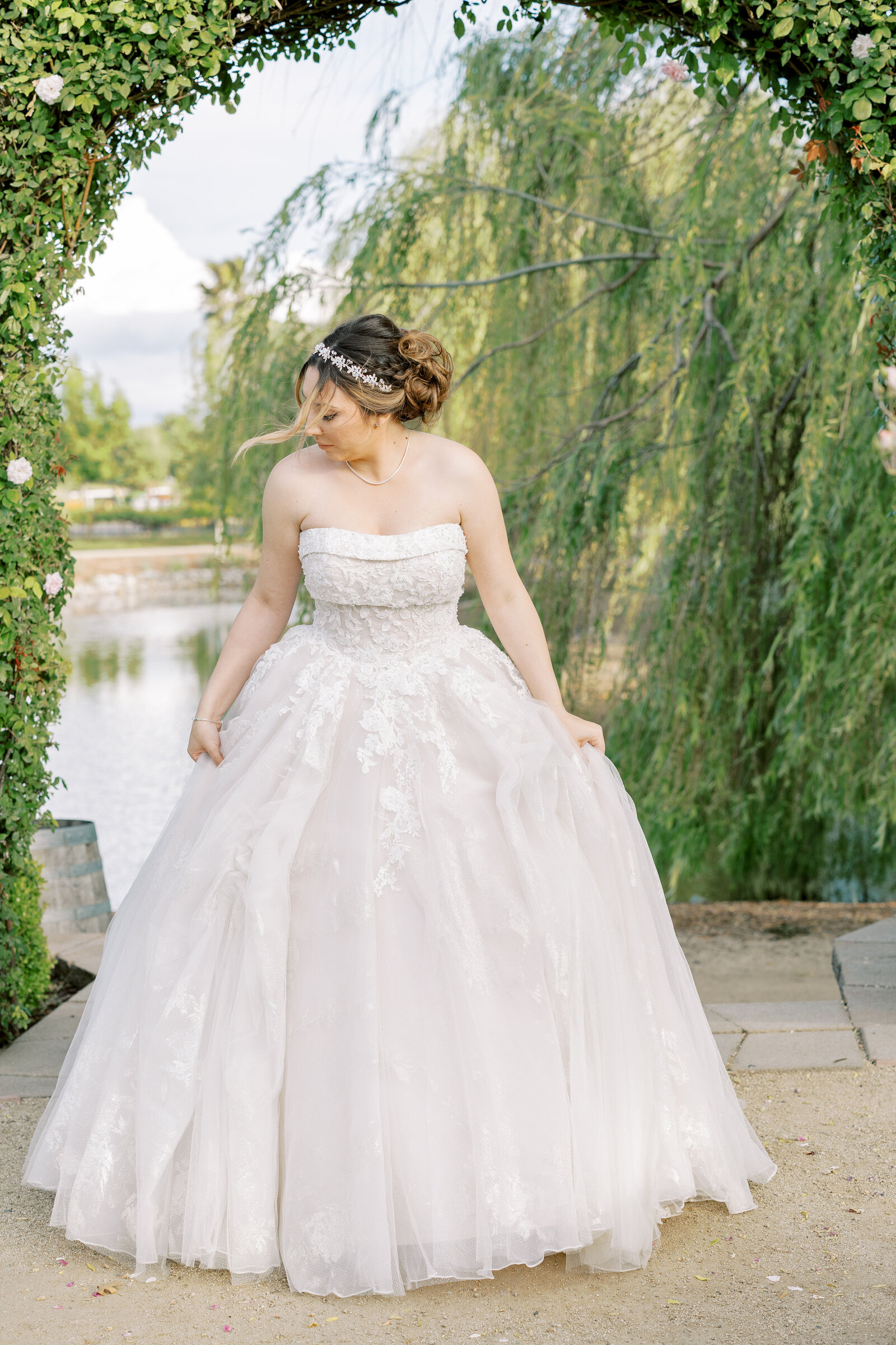 sacramento wedding photographer captures bride standing next to a lake at Wolfe Heights for her bridal portraits twirling in her wedding gown with a courtyard of hedges surrounding her