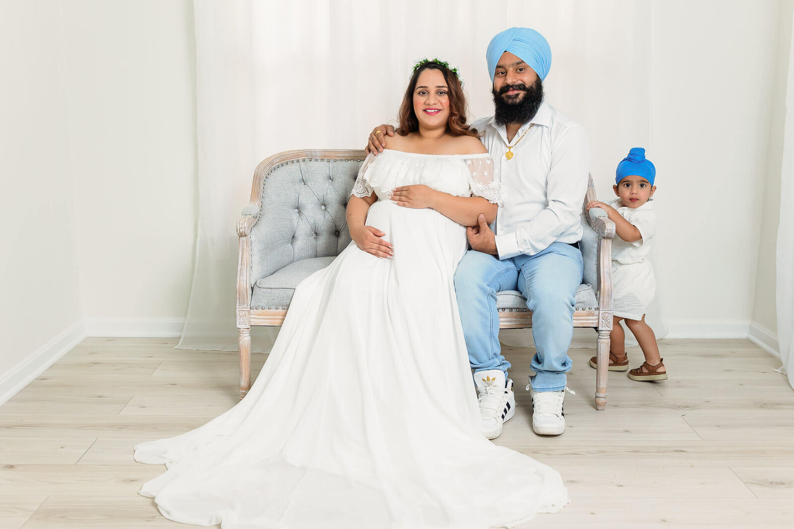 A pregnant woman and her husband and son sitting on a bench in a Gainesville, VA studio.
