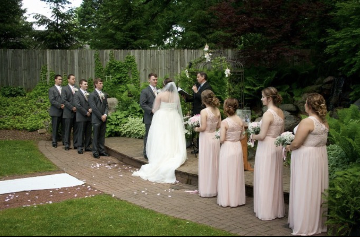 Bride and groom hold hands as their wedding parties look on in outdoor wedding ceremony